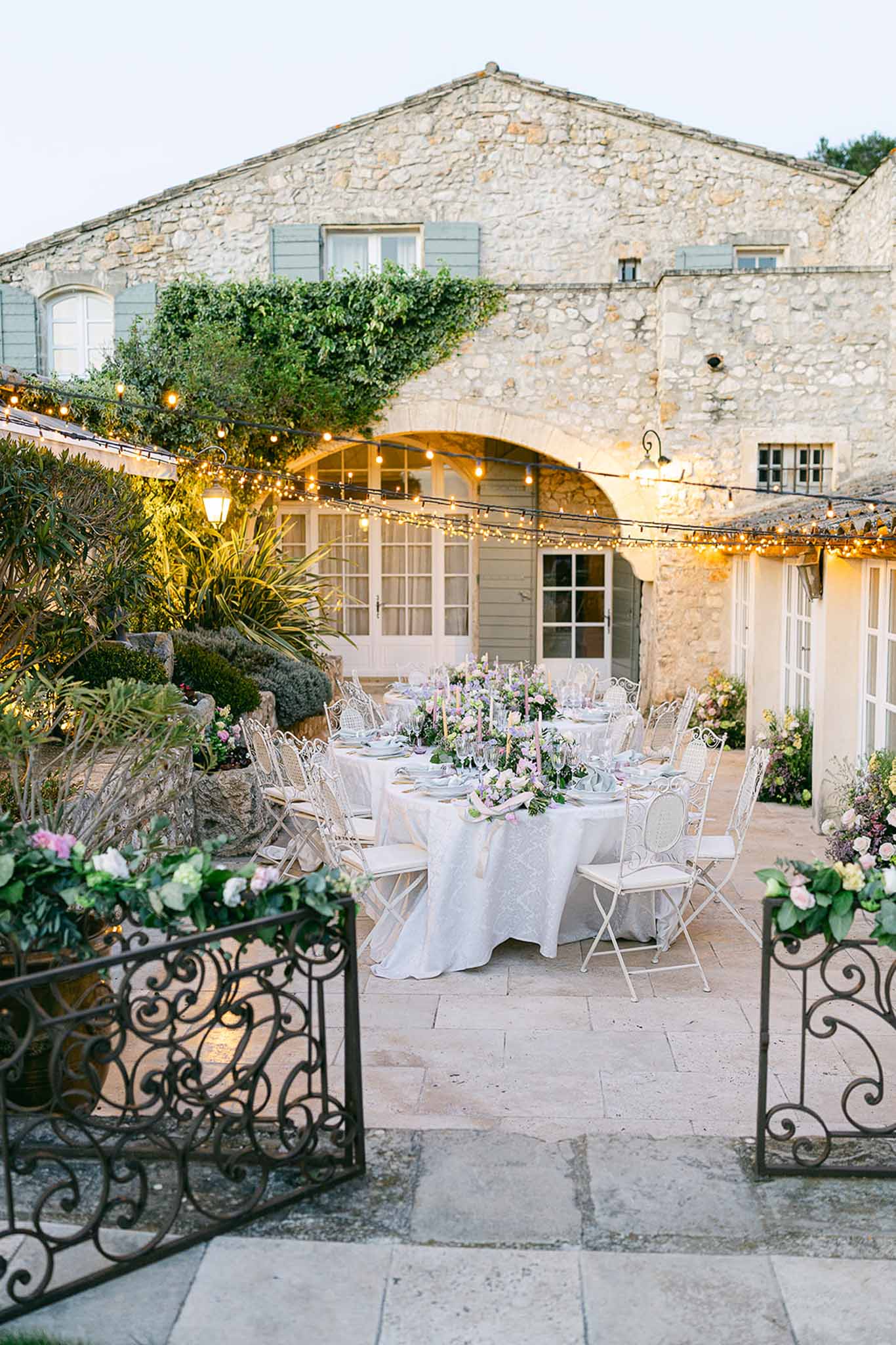 Wedding reception setup in stone courtyard of historic farmhouse with string lights and floral centerpieces