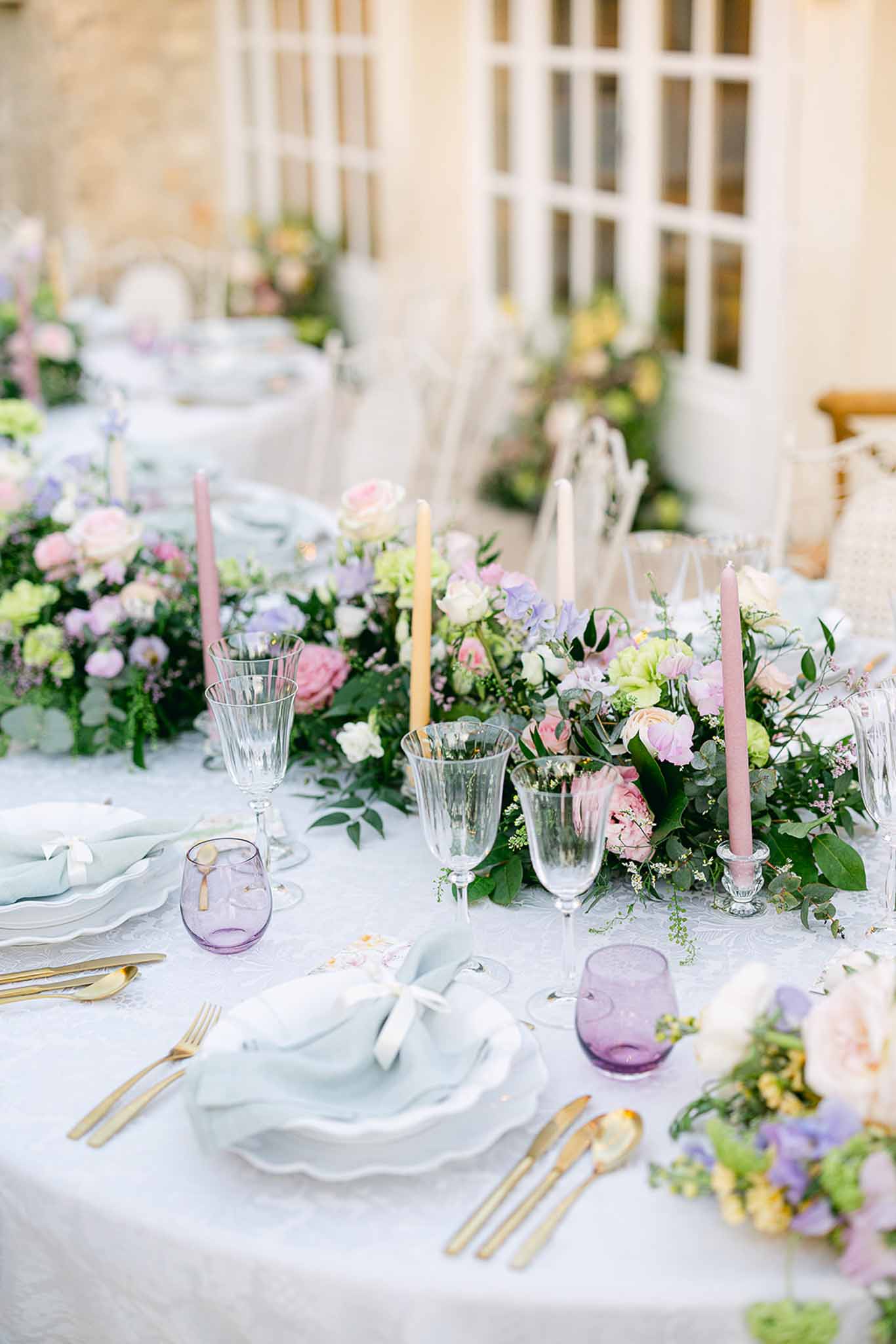 Reception table setting with floral runner and candles in stone courtyard with white latticed windows