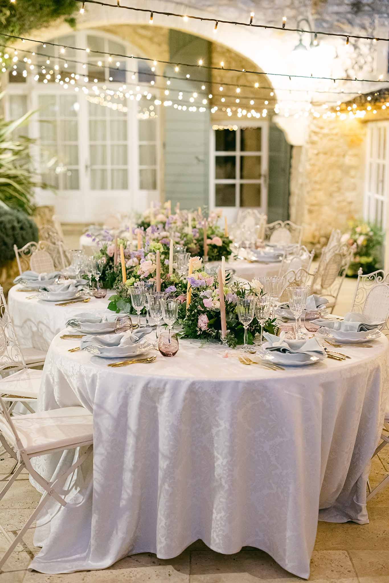 Reception dinner table setup with floral runners and candles in stone courtyard with historic building backdrop