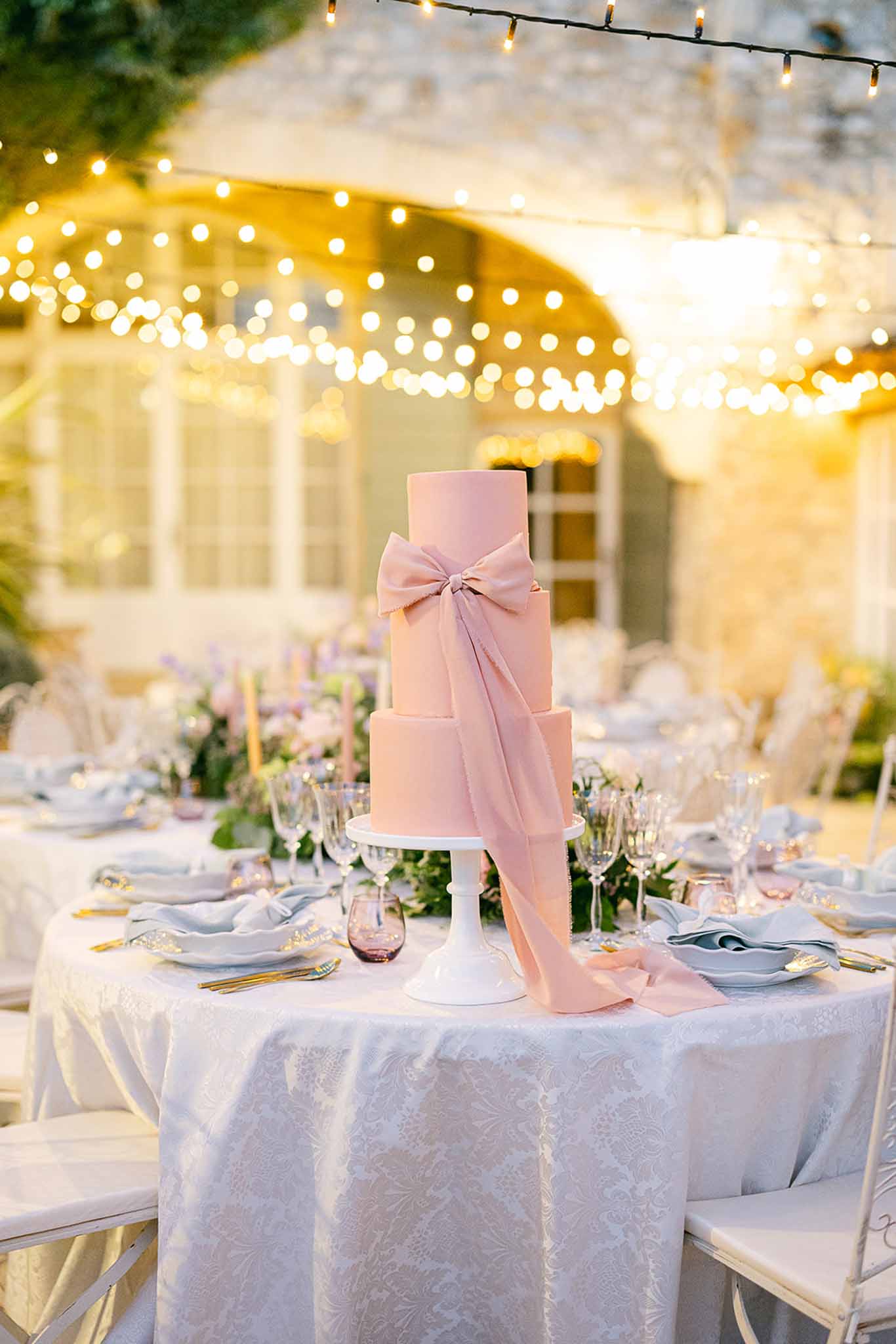 Wedding cake with blush frosting and dusty rose ribbon at outdoor marquee reception