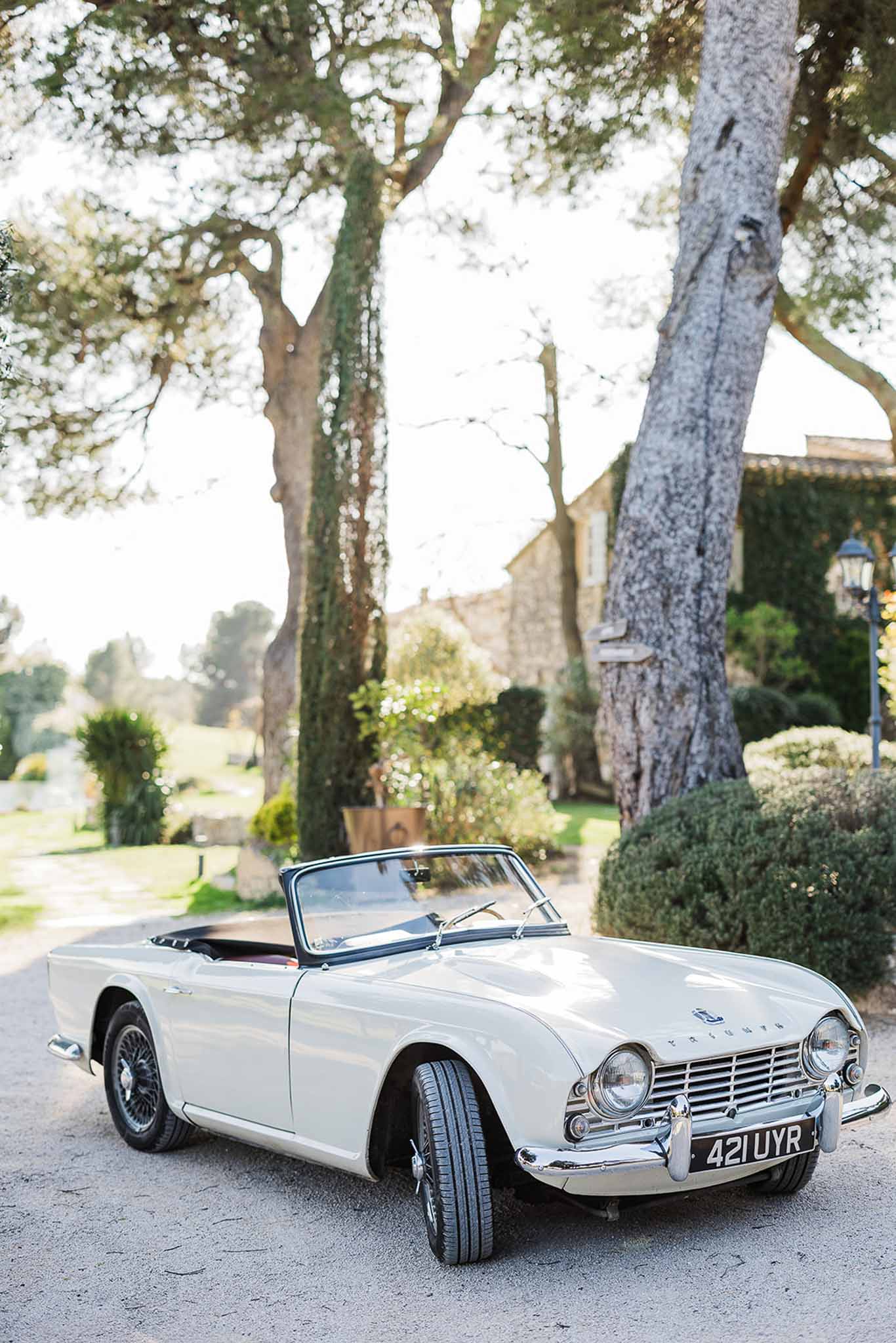 Classic white convertible sports car parked on tree-lined driveway at grand estate wedding venue