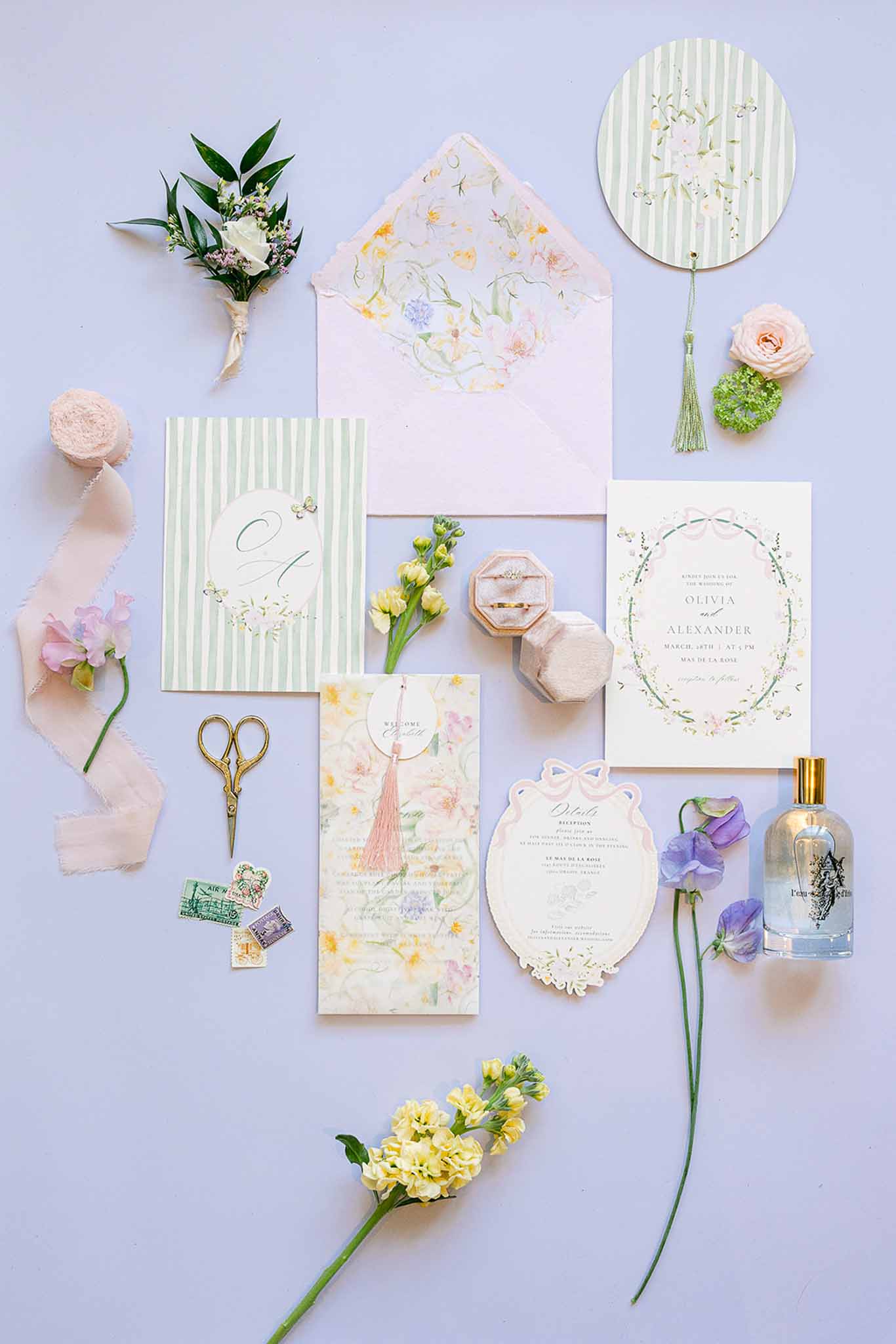Wedding stationery flat lay with blush envelopes, botanical invitations, and fresh flowers on lavender background