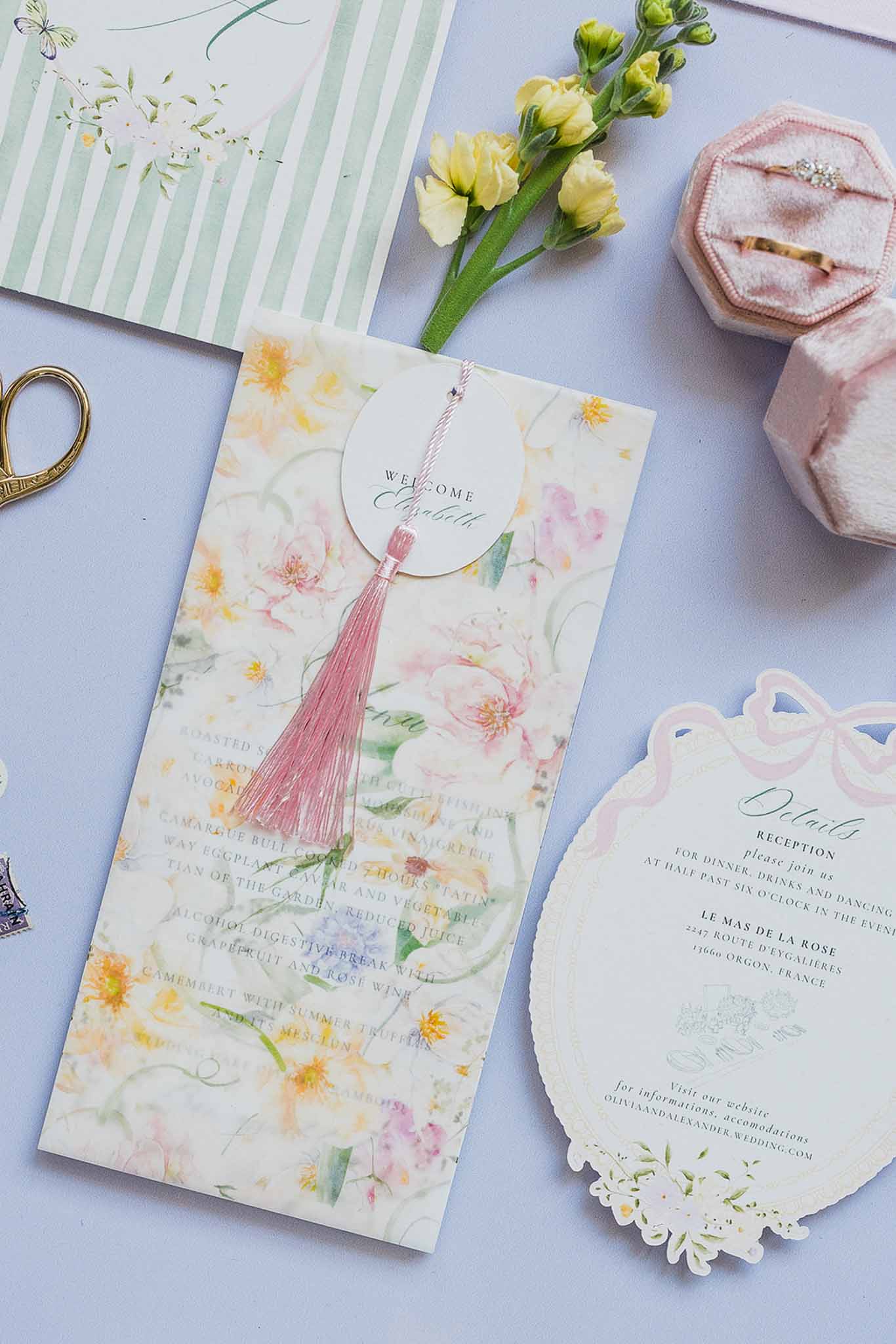 Wedding stationery flat lay with watercolor invitations and blush pink accessories on lavender surface