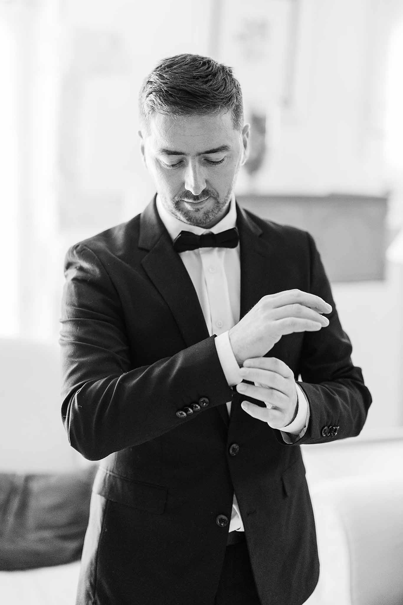 Groom adjusting cufflinks in black tuxedo during getting ready preparations