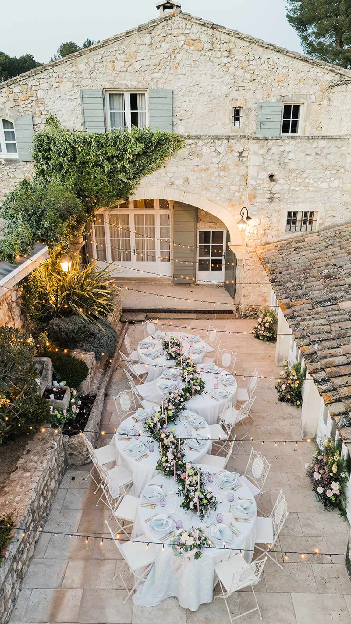 Aerial view of wedding reception table setup in historic stone courtyard with floral runners and string lights