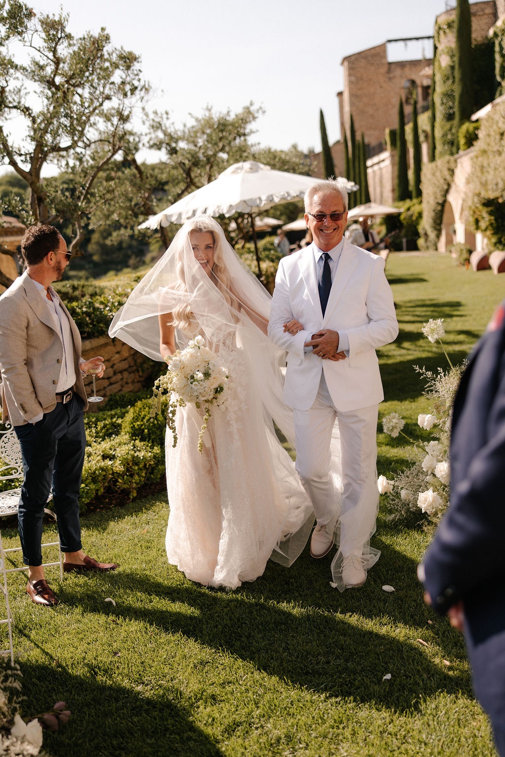 Bride walks down aisle with father beneath parasol at Airelles Gordes La Bastide, Provence
