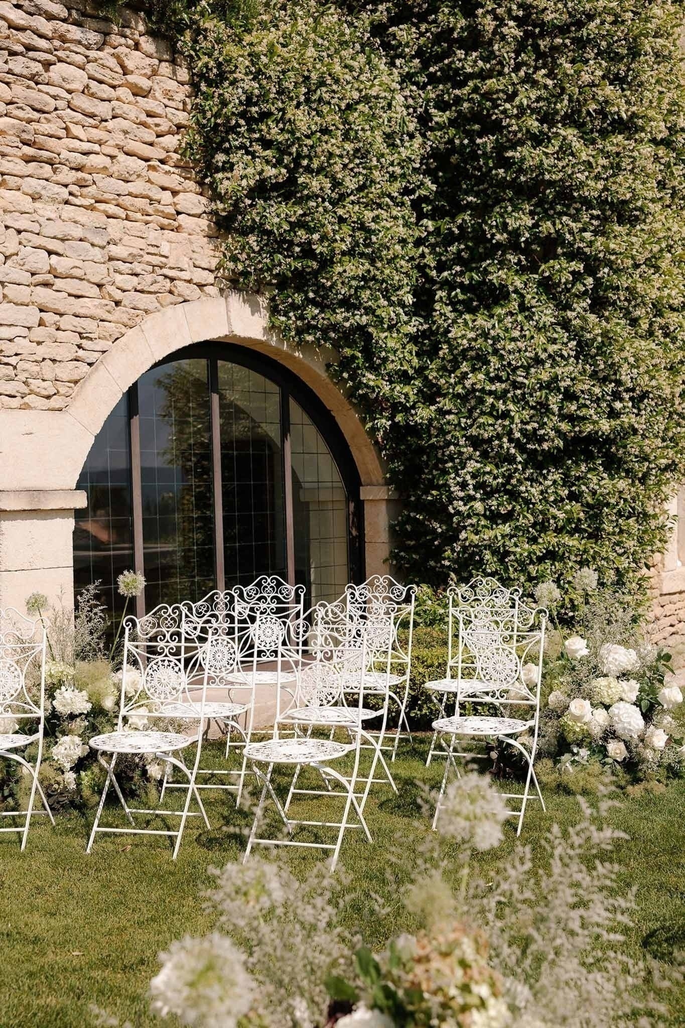 Ceremony chairs with white florals beside jasmine arch at Airelles Gordes La Bastide