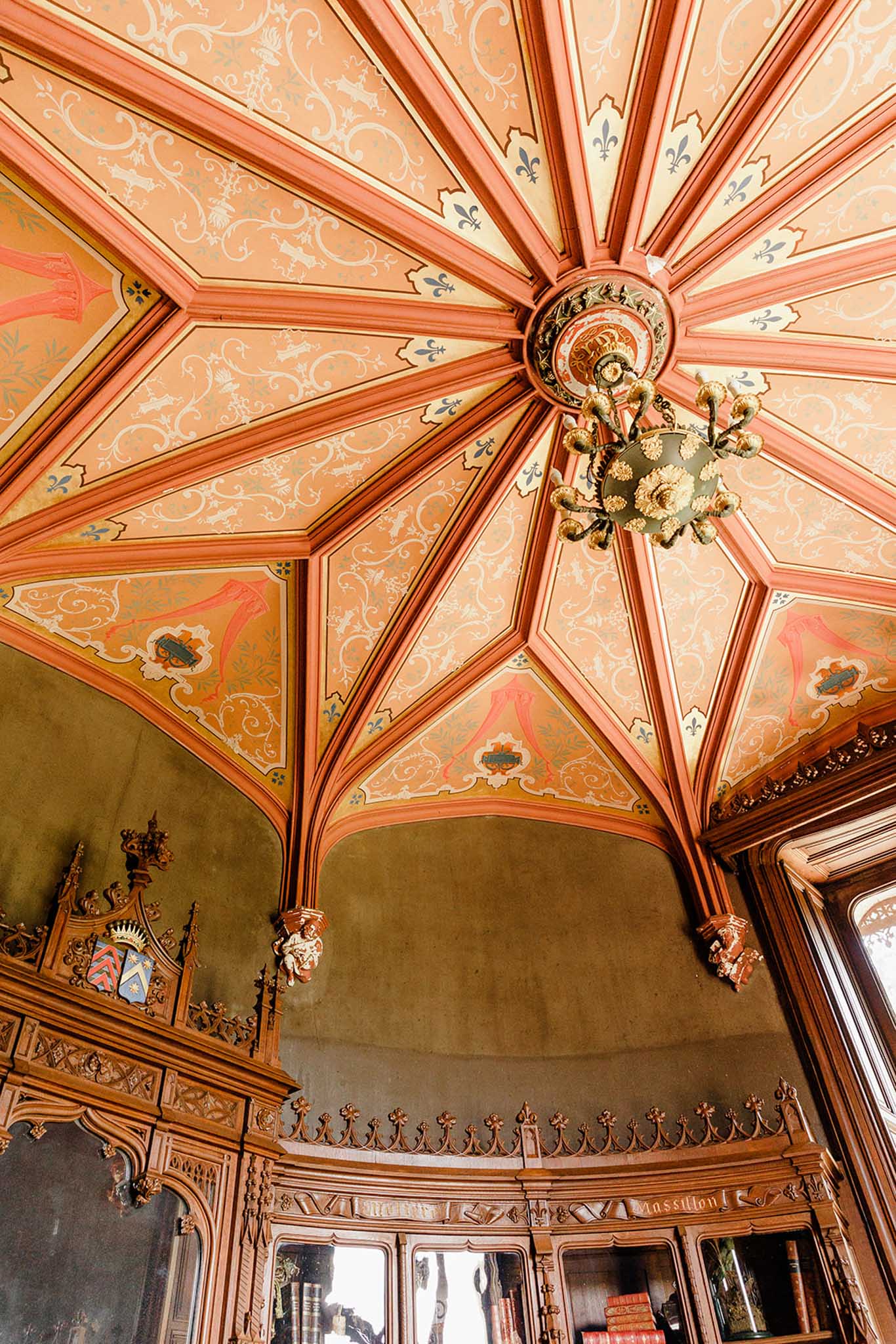 Fan-vaulted ceiling with terracotta ribbing, heraldic shields, and Gothic carved wood paneling inside Chateau Challain