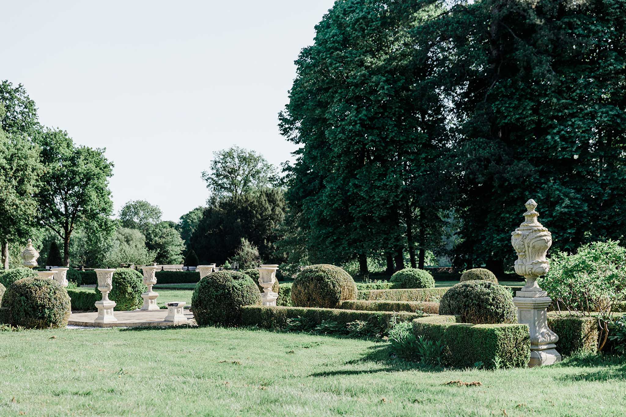Formal French garden with symmetrical boxwood hedges, stone urns on pedestals, and geometric pathways