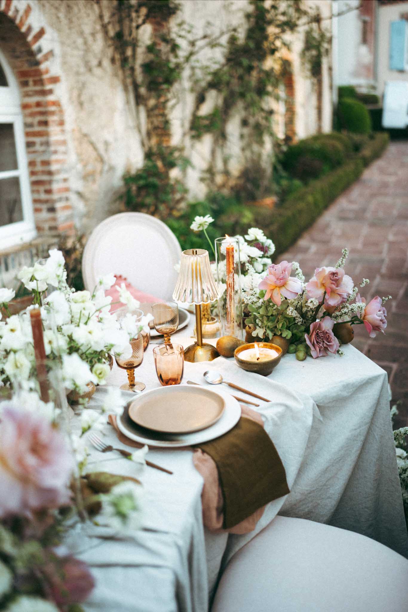 Elegant table setting with floral centerpieces and gold accents in European courtyard