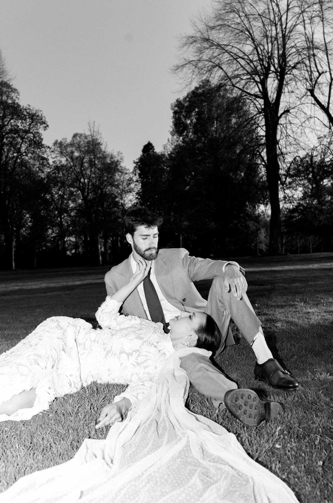 Bride and groom relaxing on lawn in romantic black and white portrait at garden wedding venue