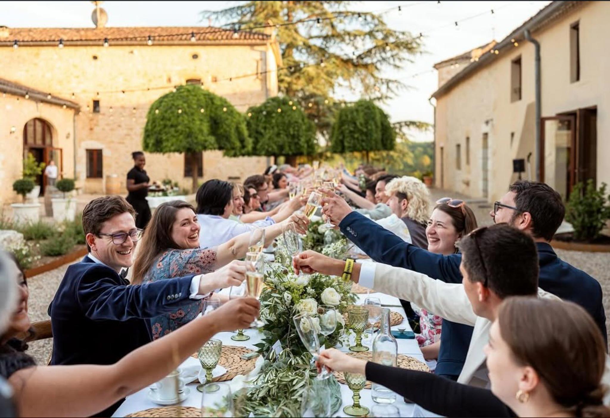 Guests toasting champagne at banquet table with peony and eucalyptus garland sage glassware and string lights