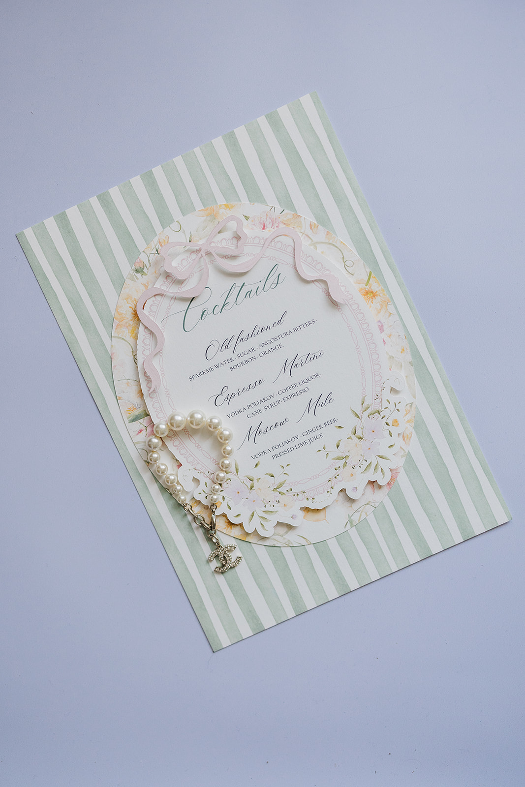 Cocktail menu card with sage stripe and watercolor floral border and pearl Chanel charm bracelet