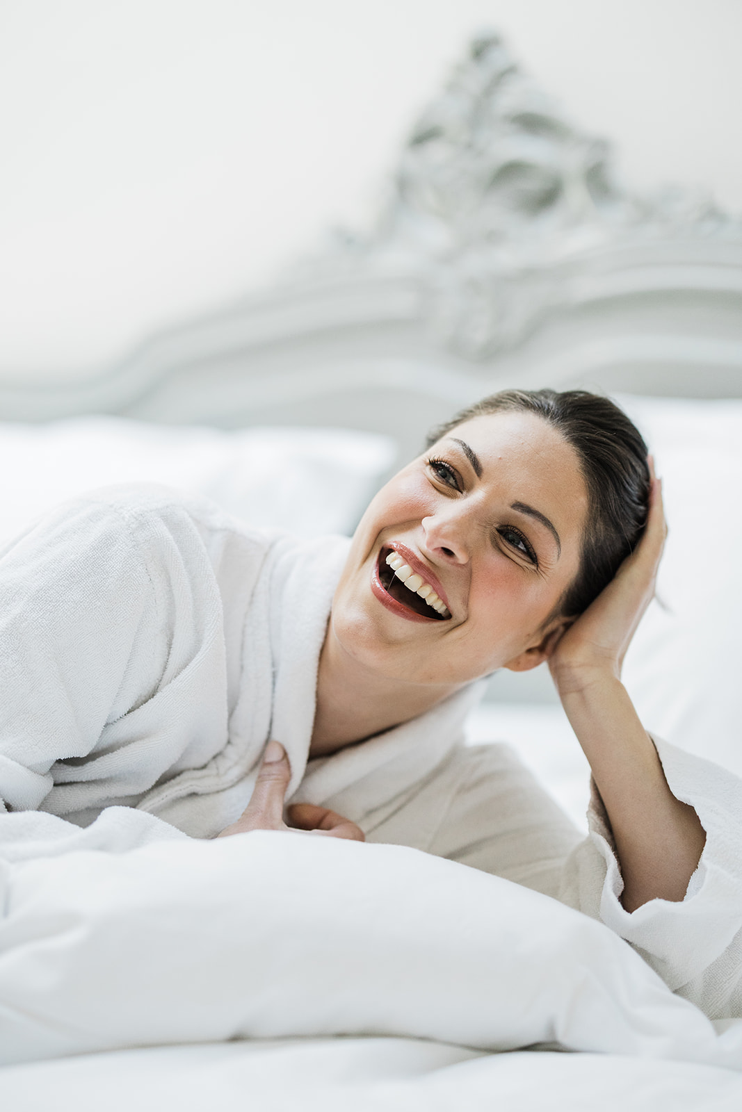 Bride in white robe during getting ready preparation with wedding dress in background