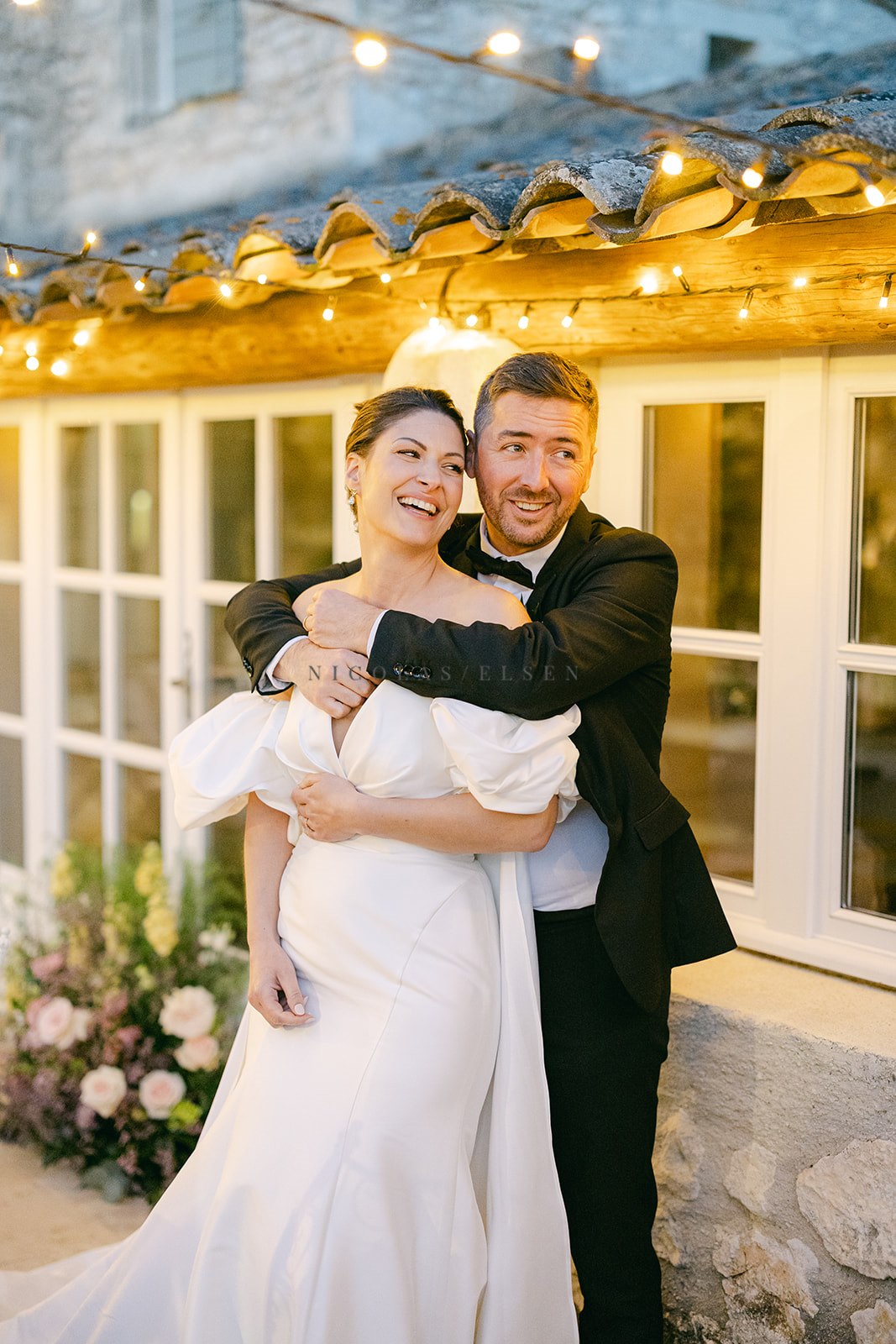 Laughing couple embracing under string lights at Provencal stone venue in evening light