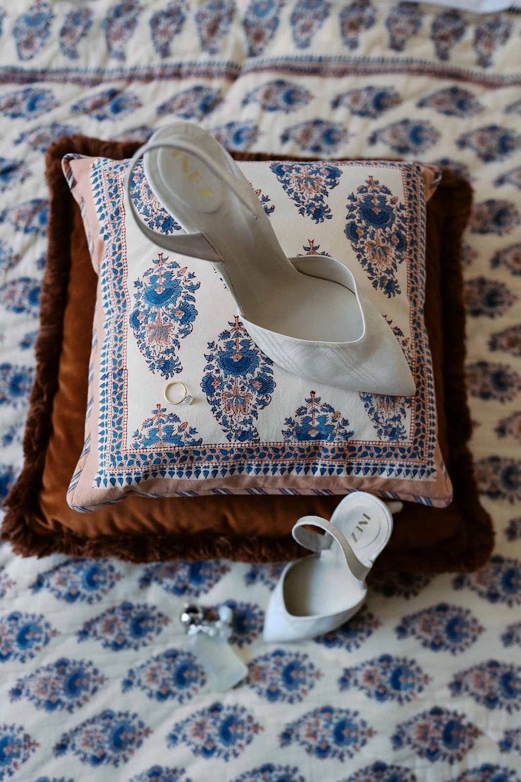Pointed white bridal slingbacks and earrings arranged on a block-print cushion at the hotel before the wedding