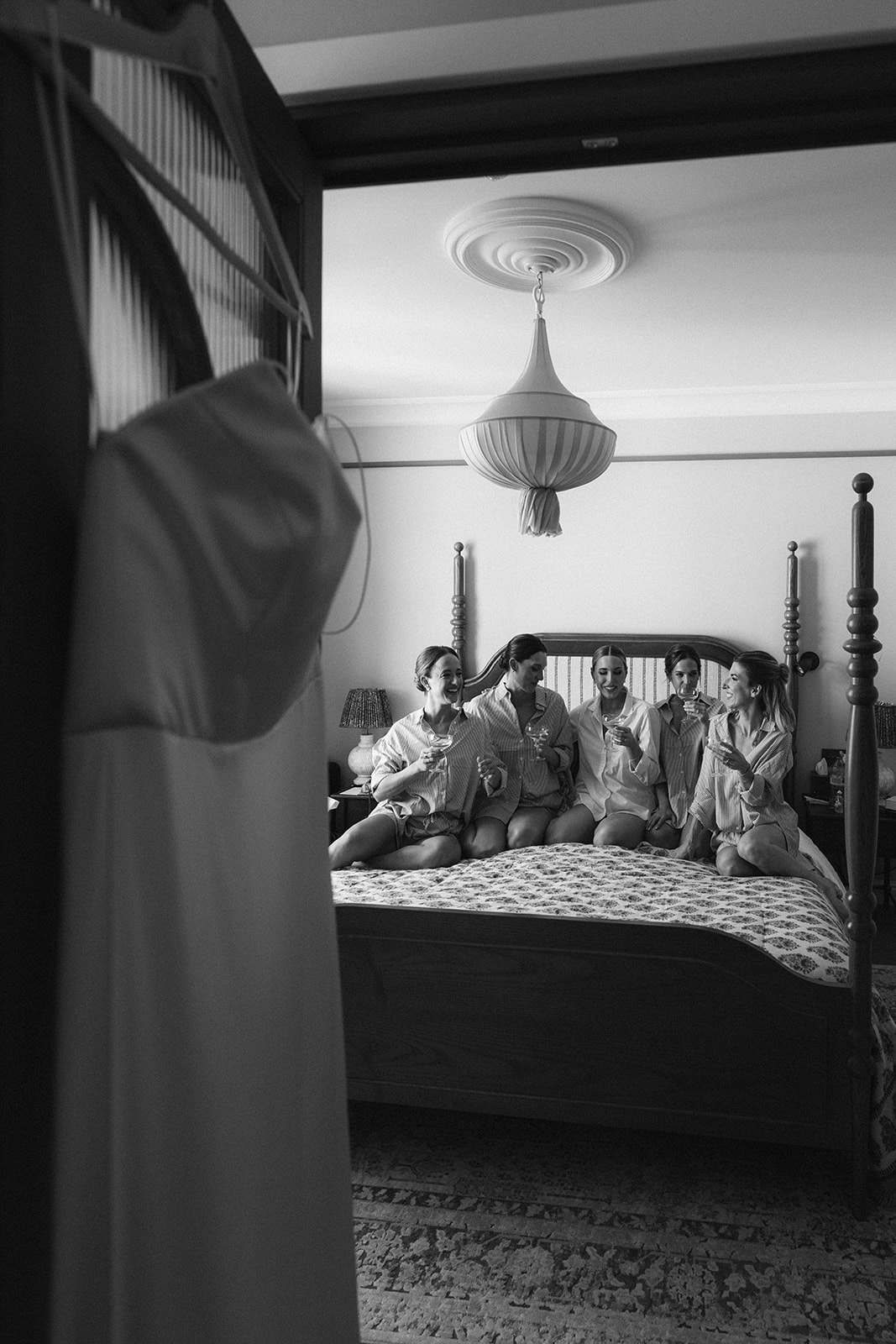 Black and white shot of bridesmaids on a hotel bed in Paris while the dress hangs in the foreground