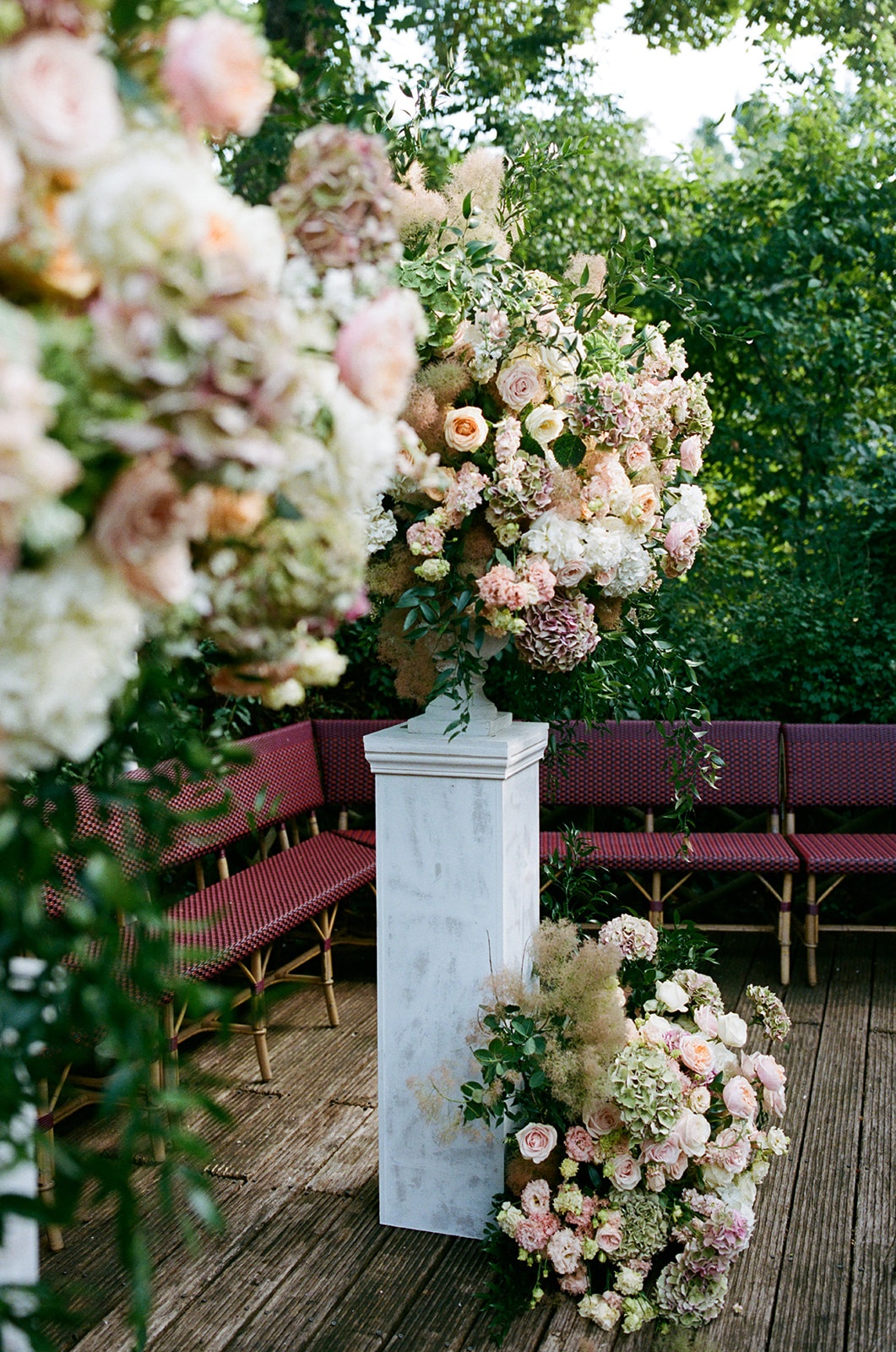 Tall blush and ivory ceremony floral arrangement on a marble plinth with bistro benches