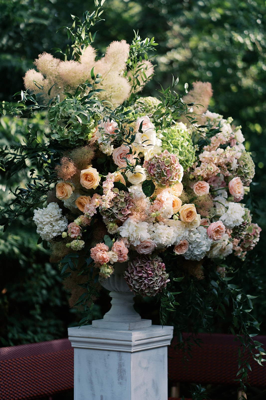 Tall ceremony arrangement of garden roses, hydrangea, and smoke bush in a marble urn