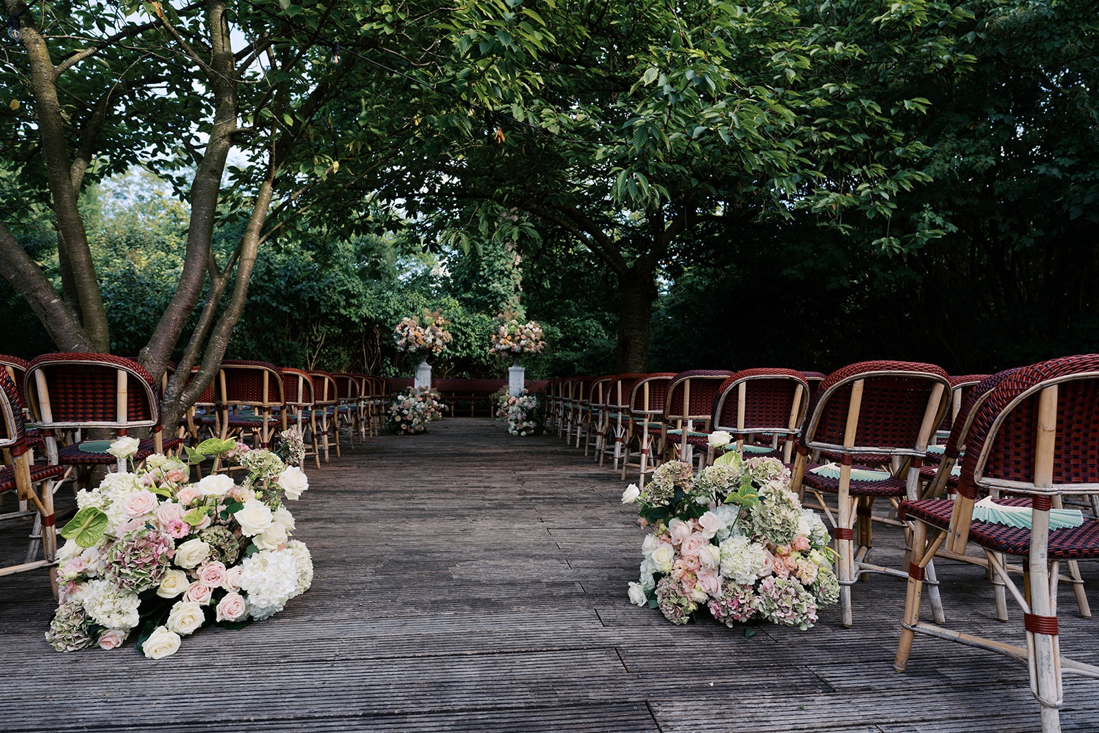 Outdoor ceremony aisle at Restaurant l'Ile with red bistro chairs, blush florals, and the altar at the end