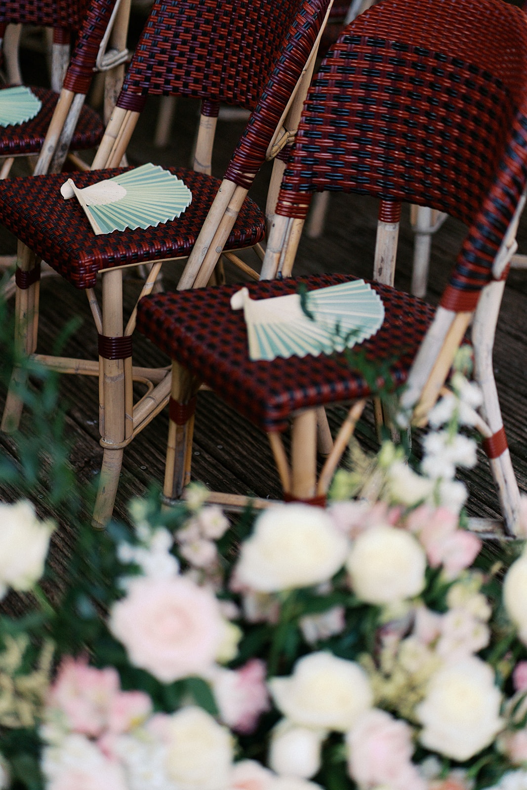 Sage green paper hand fans on red Parisian bistro ceremony chairs with blush florals
