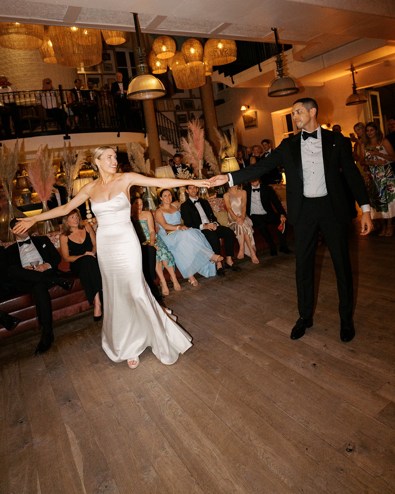 Couple's first dance under woven pendant lights with seated guests and pampas grass behind