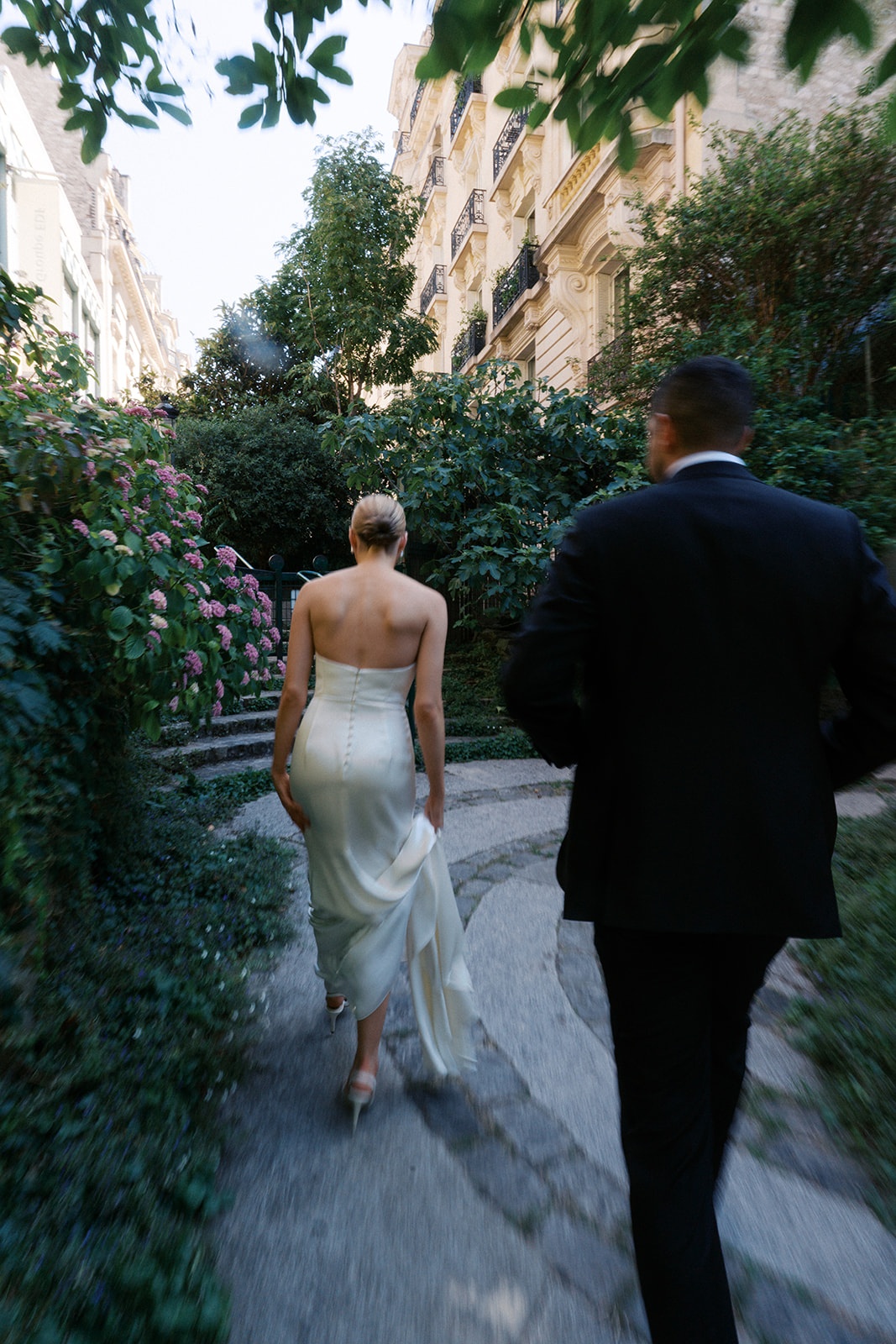 Couple walking away down a leafy Paris pathway beside flowering hydrangea