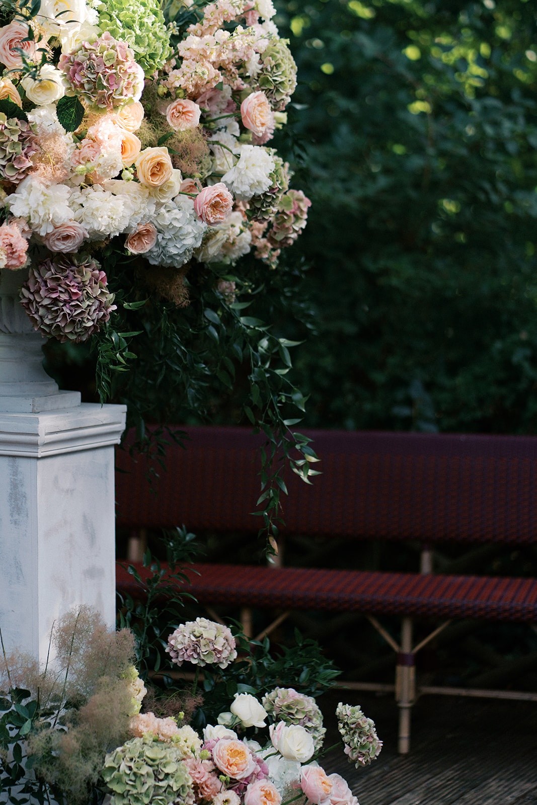 Floral pillar in a marble urn with a red bistro bench and cascading garden roses