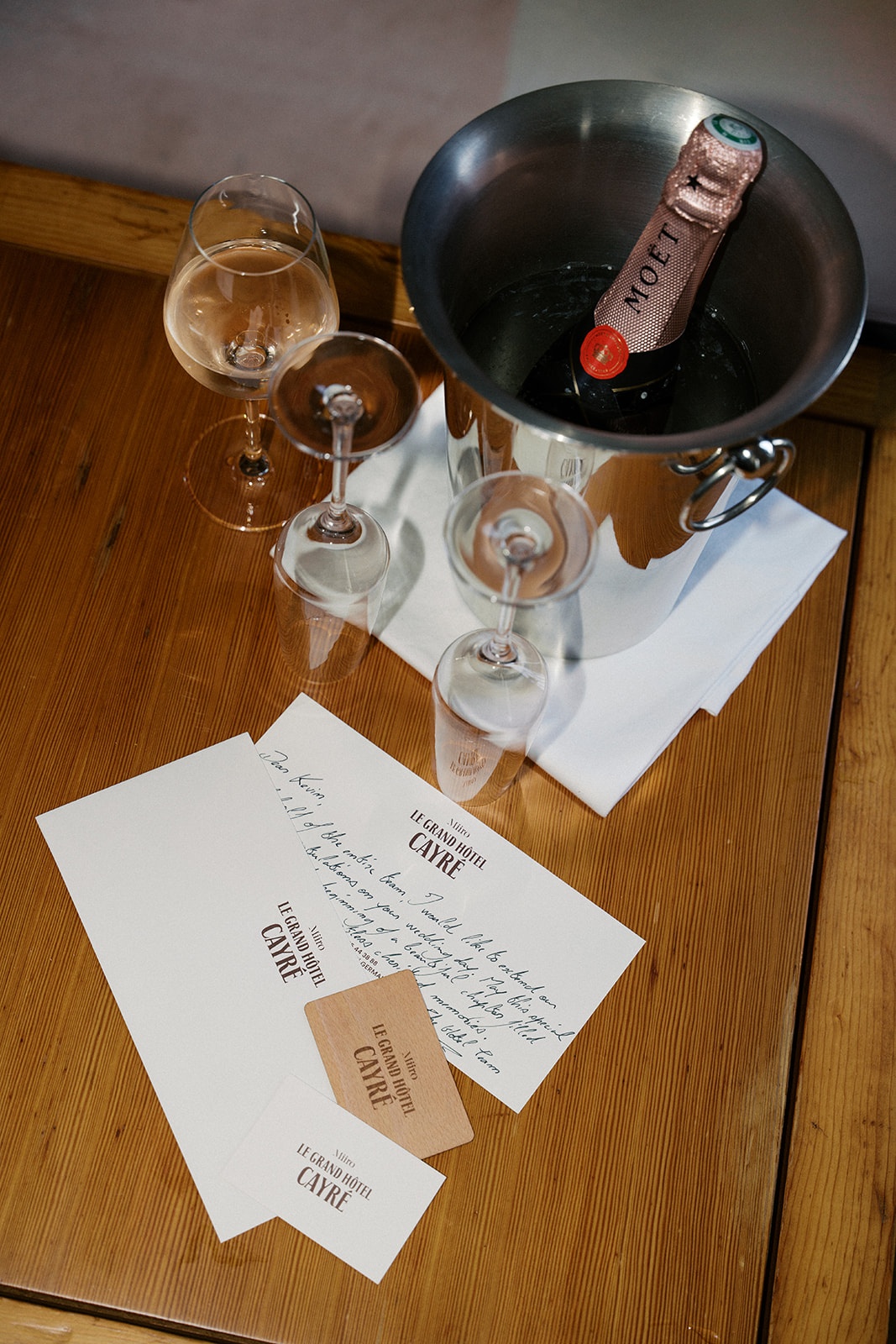 Moet rose champagne, coupe glasses, and a handwritten Le Grand Hotel Cayre note on a wooden table