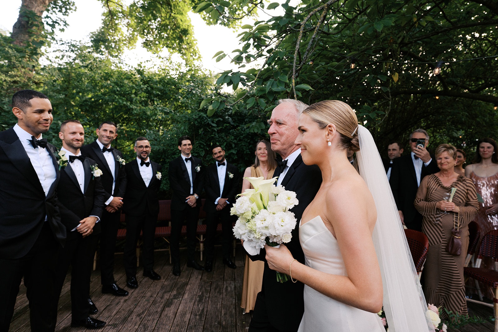 Bride with her father at the aisle, groomsmen lined up in tuxedos and the groom waiting