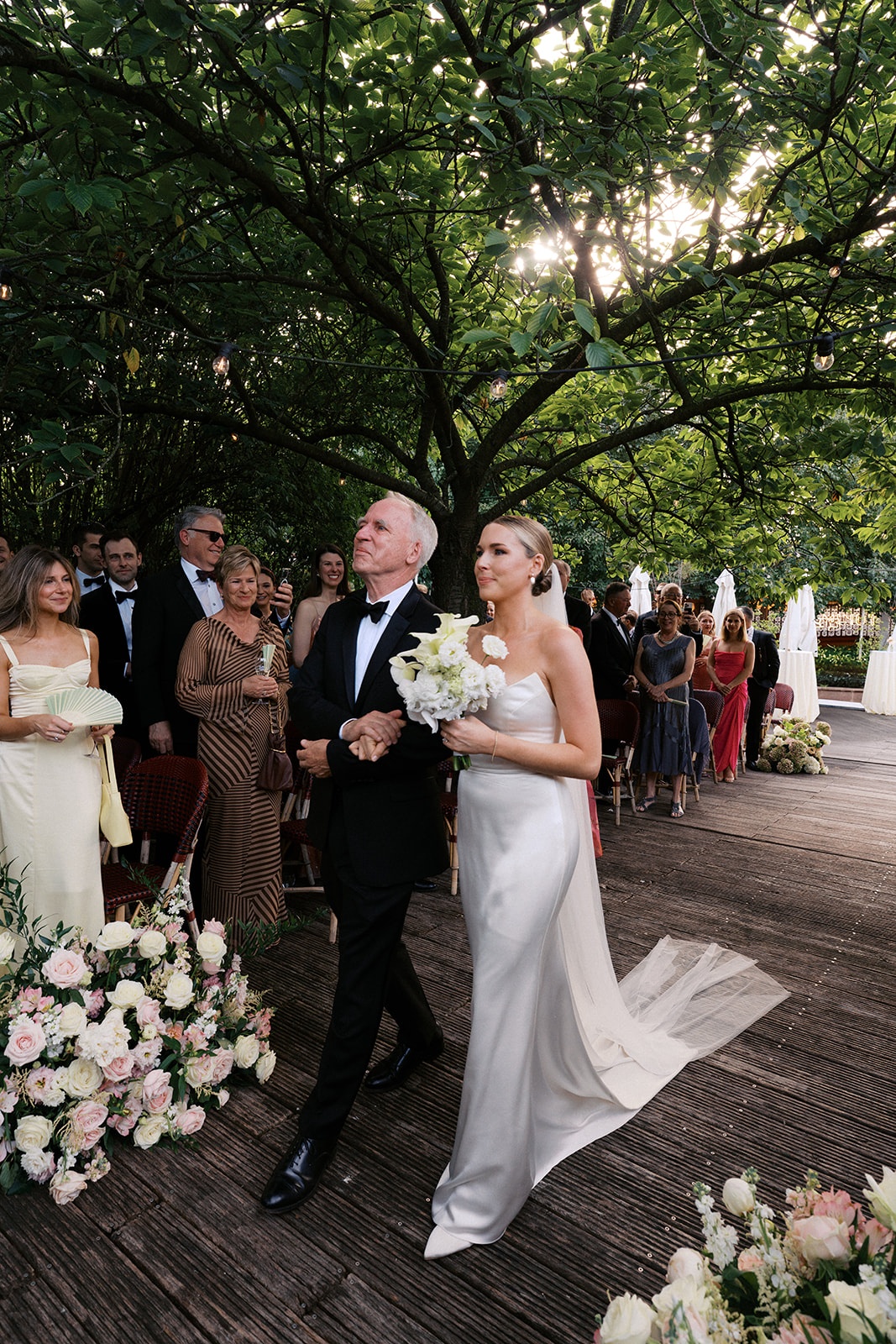 Bride walks down the aisle on her father's arm beneath a leafy canopy at Restaurant l'Ile