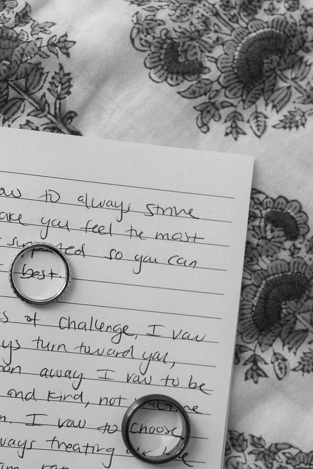 Black and white flat lay of two wedding bands resting on a handwritten vows page