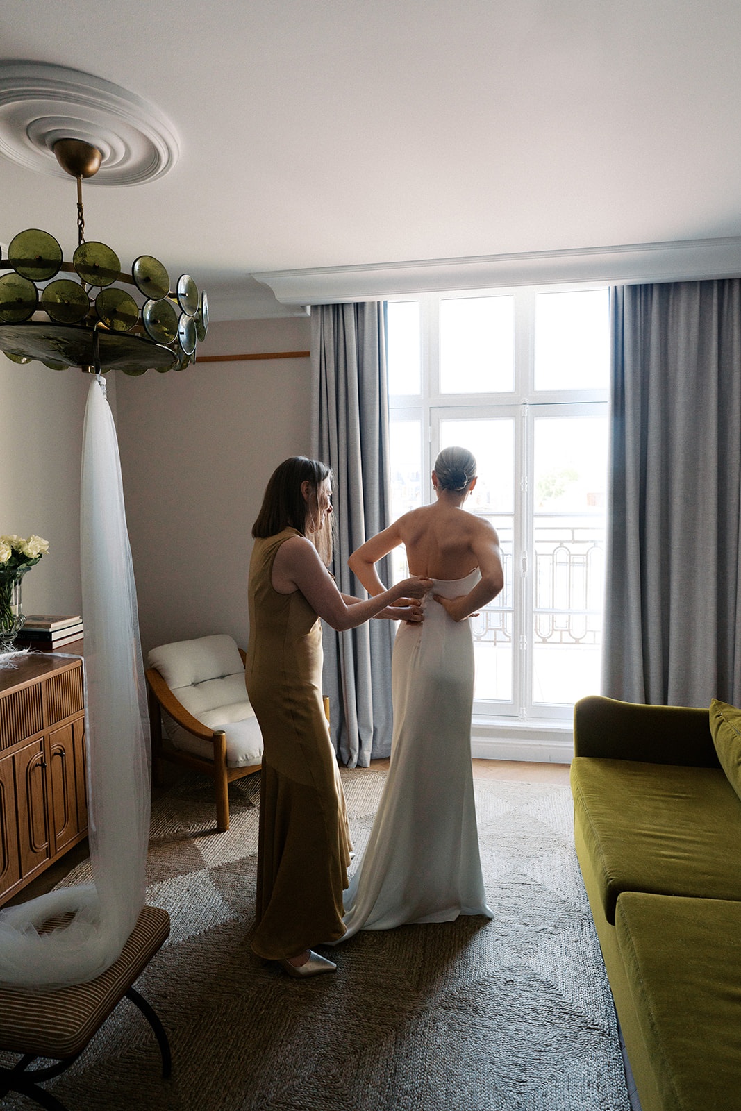 Bride being fastened into her ivory column gown by a bridesmaid in a Paris hotel suite