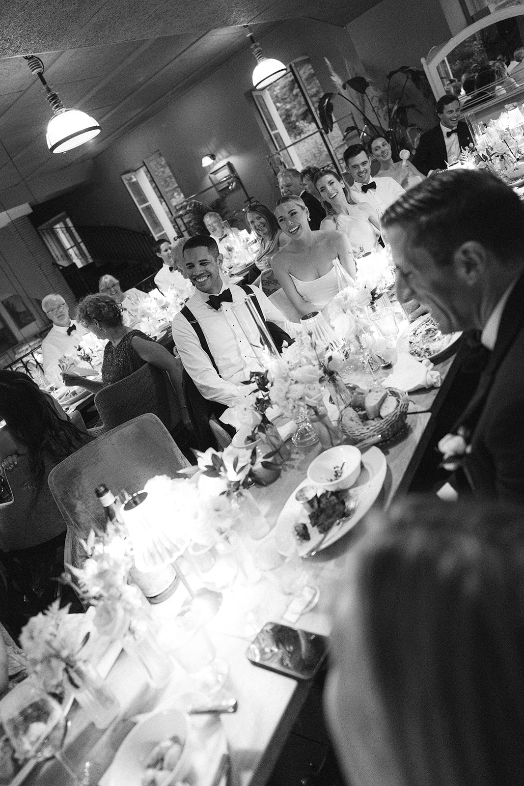 Black and white reception speech with the bride, groom, and seated guests at the long table