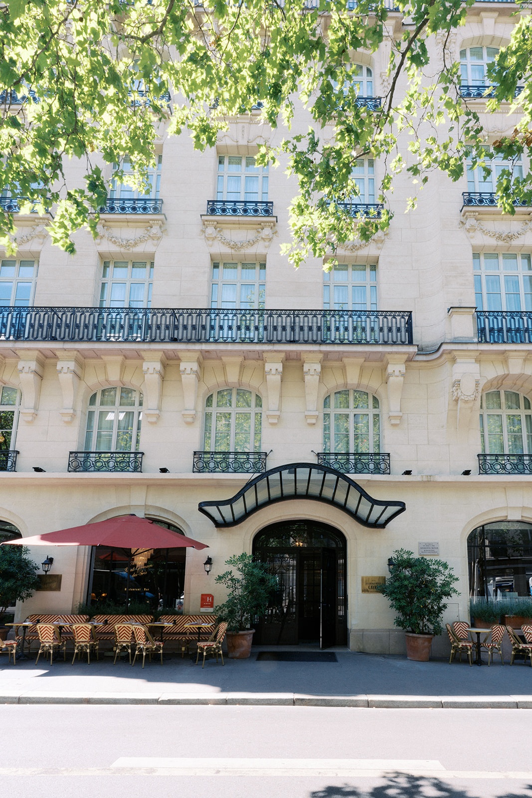 Stone facade of Le Grand Hotel Cayre in Paris with red and white bistro chairs at the cafe