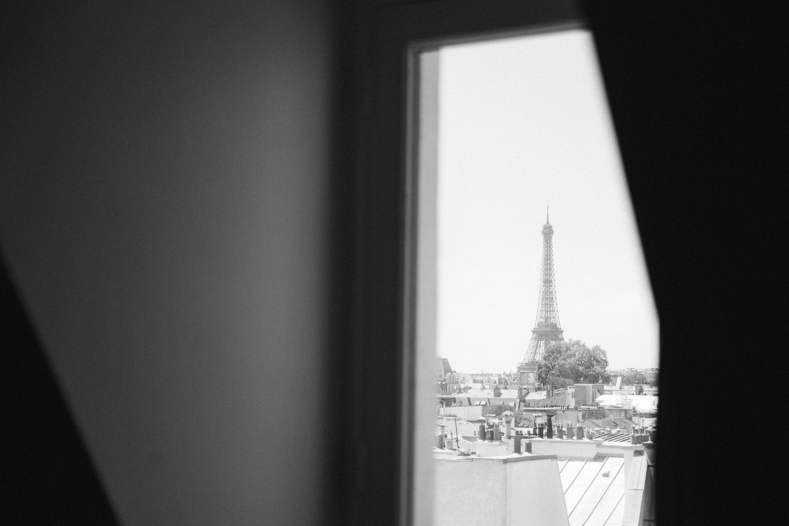 Black and white view of the Eiffel Tower through a hotel window across Paris rooftops