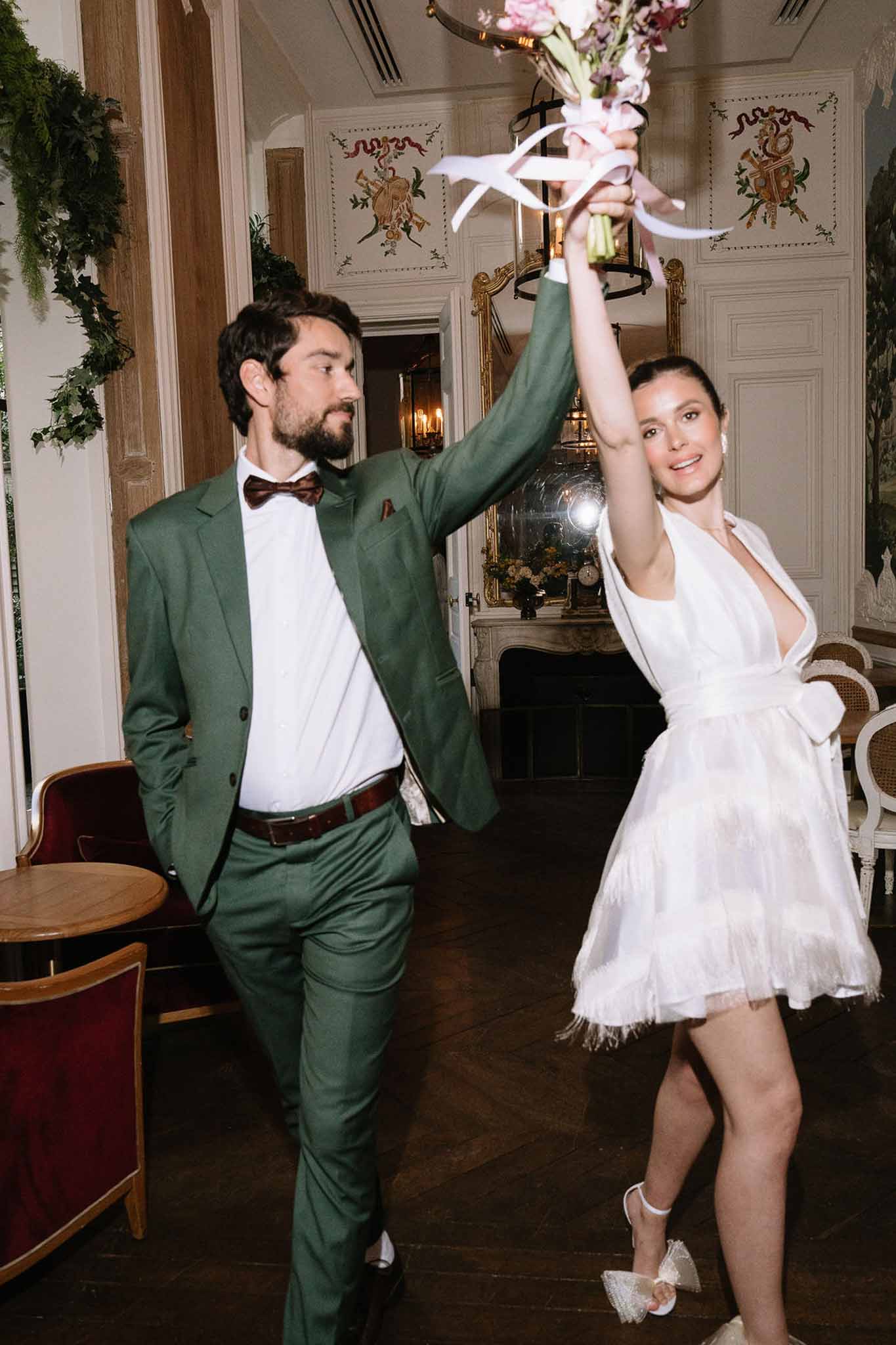 Couple dancing through panelled reception room bride in white fringed mini dress groom in forest green suit with burgundy ...