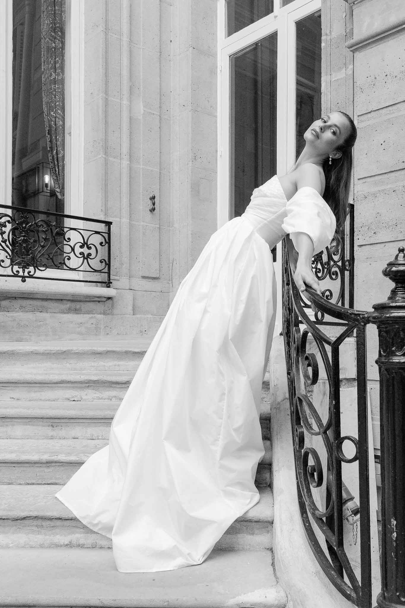 Black and white full-length bridal portrait in puff-sleeve ball gown on stone steps with iron railing