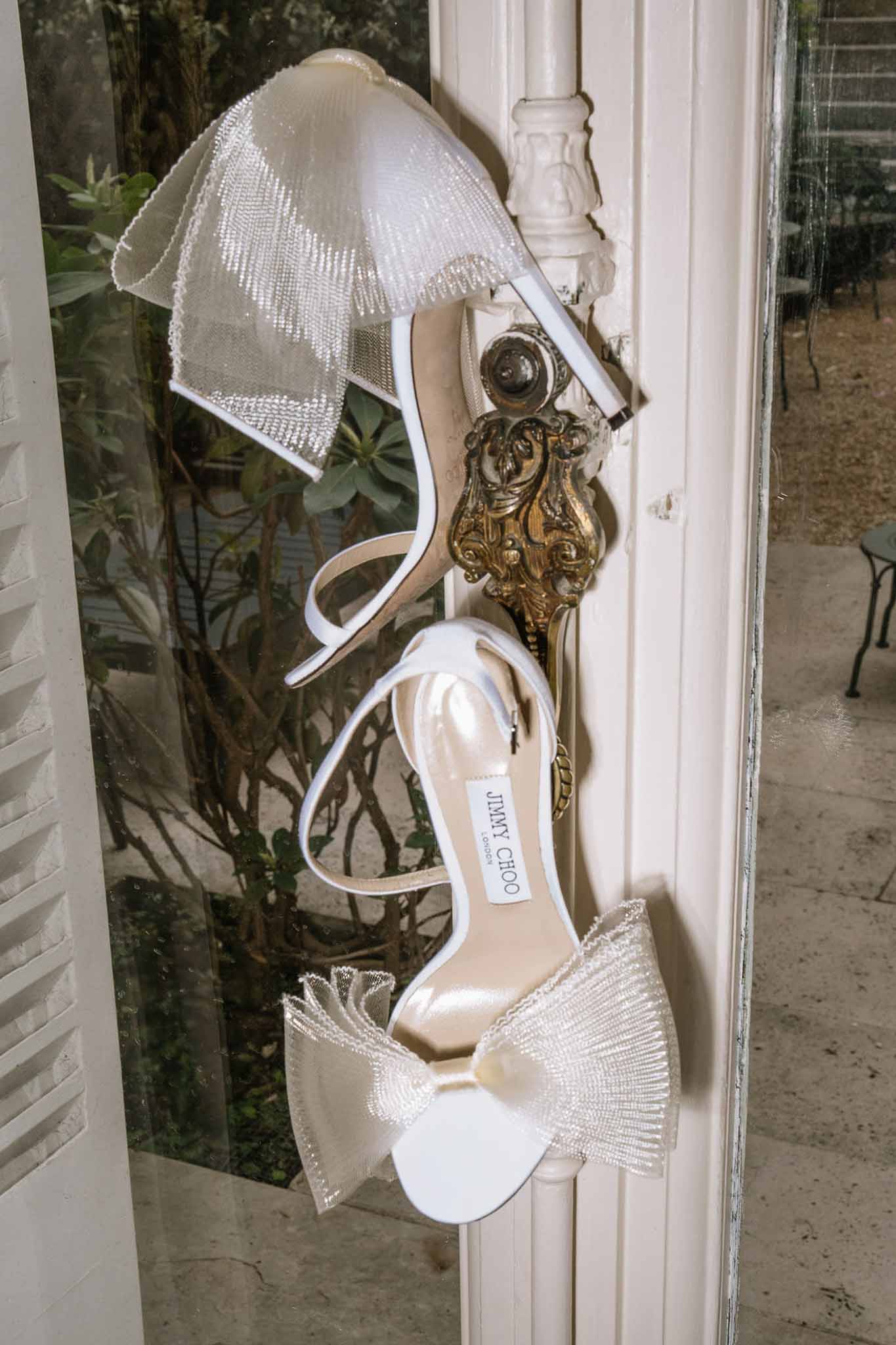 White Jimmy Choo beaded tulle bow sandals hanging from gold door handle at French venue