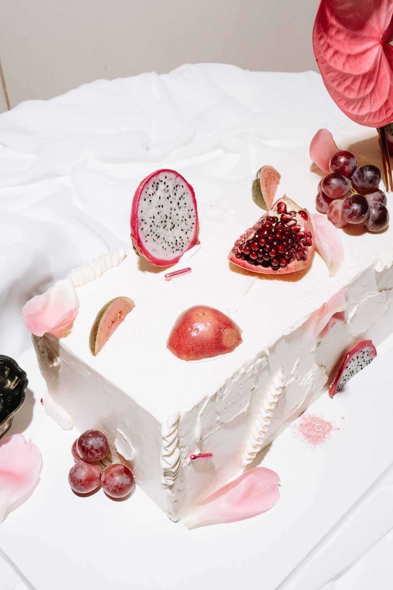 Square single-tier white buttercream cake topped with dragon fruit, pomegranate, peach, and red grapes