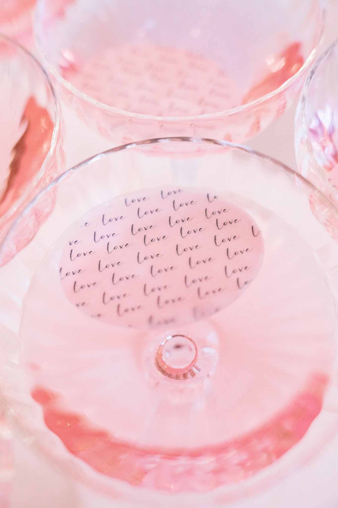 Close-up of wine glasses from above showing love script label on base with pink-tinted rose wine