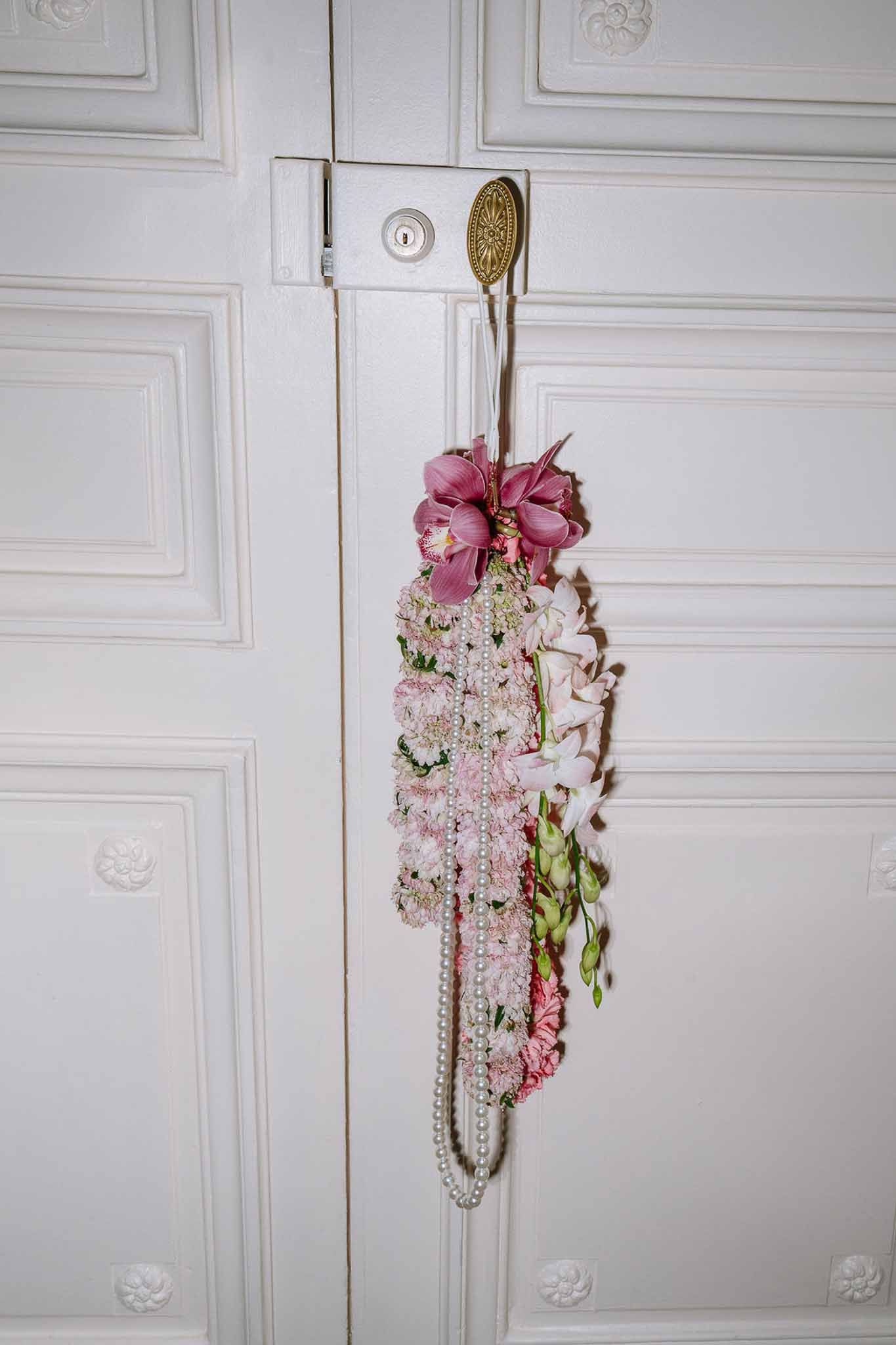Indian-style flower garland of pink carnations and orchids with pearl necklace hanging on panelled door