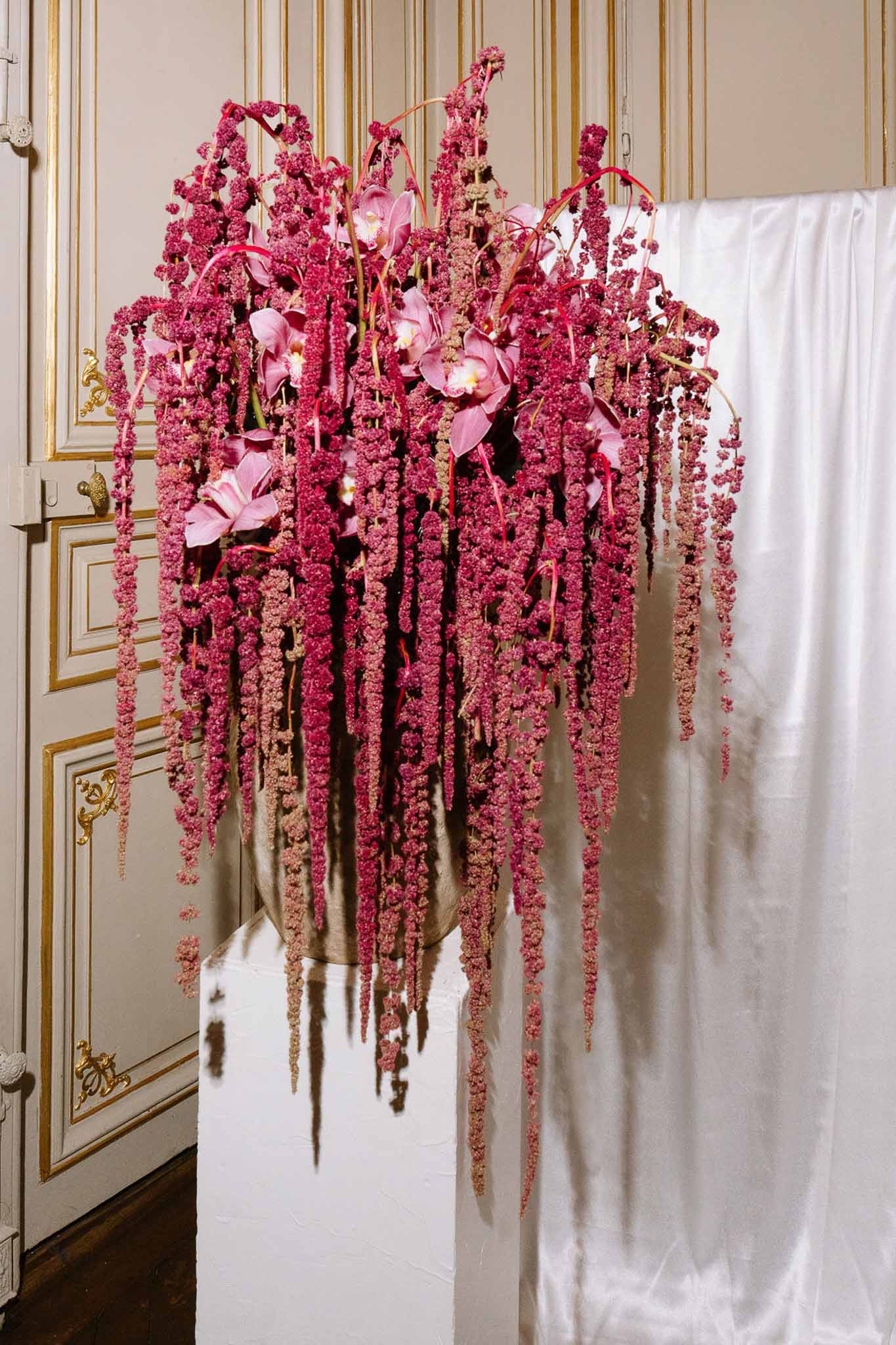 Cascading magenta amaranthus and blush cymbidium orchid arrangement in gold vase with boiserie paneling