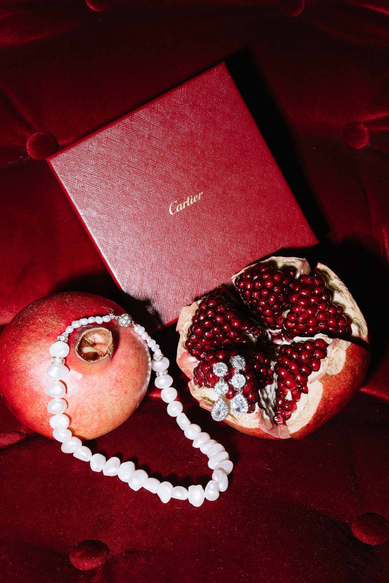 Pearl bracelet and crystal earrings styled on pomegranates beside red Cartier box