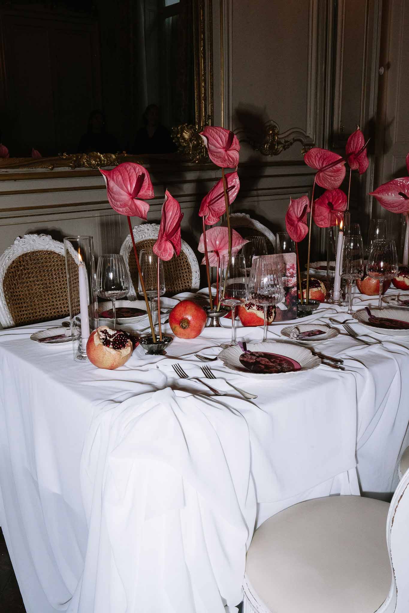Reception table with burgundy plates, hot pink anthurium centerpieces, pomegranate accents, and lit taper candles