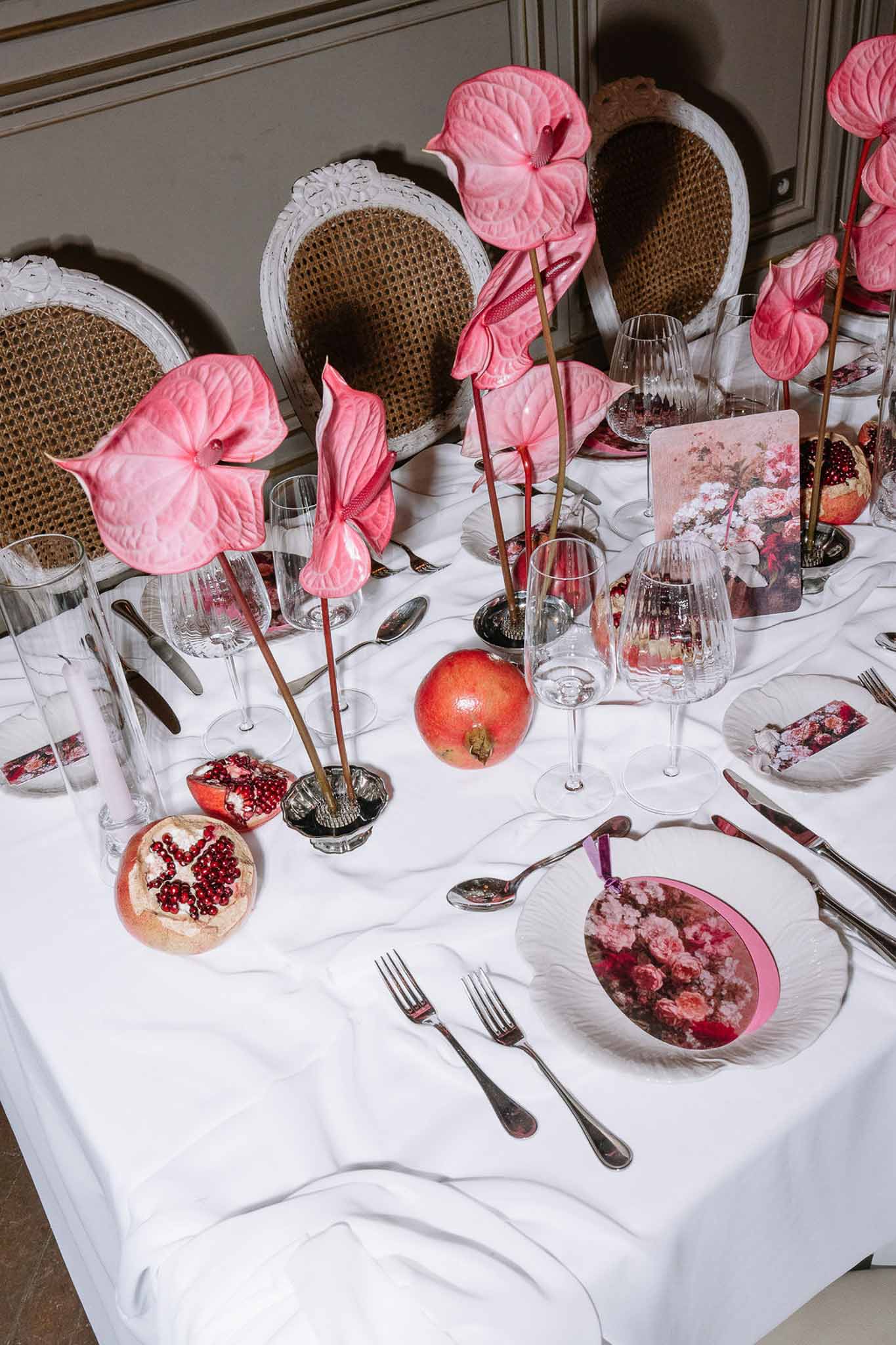 Hot pink anthurium centerpieces with halved pomegranates and floral-printed menus on white linen with cane-back chairs