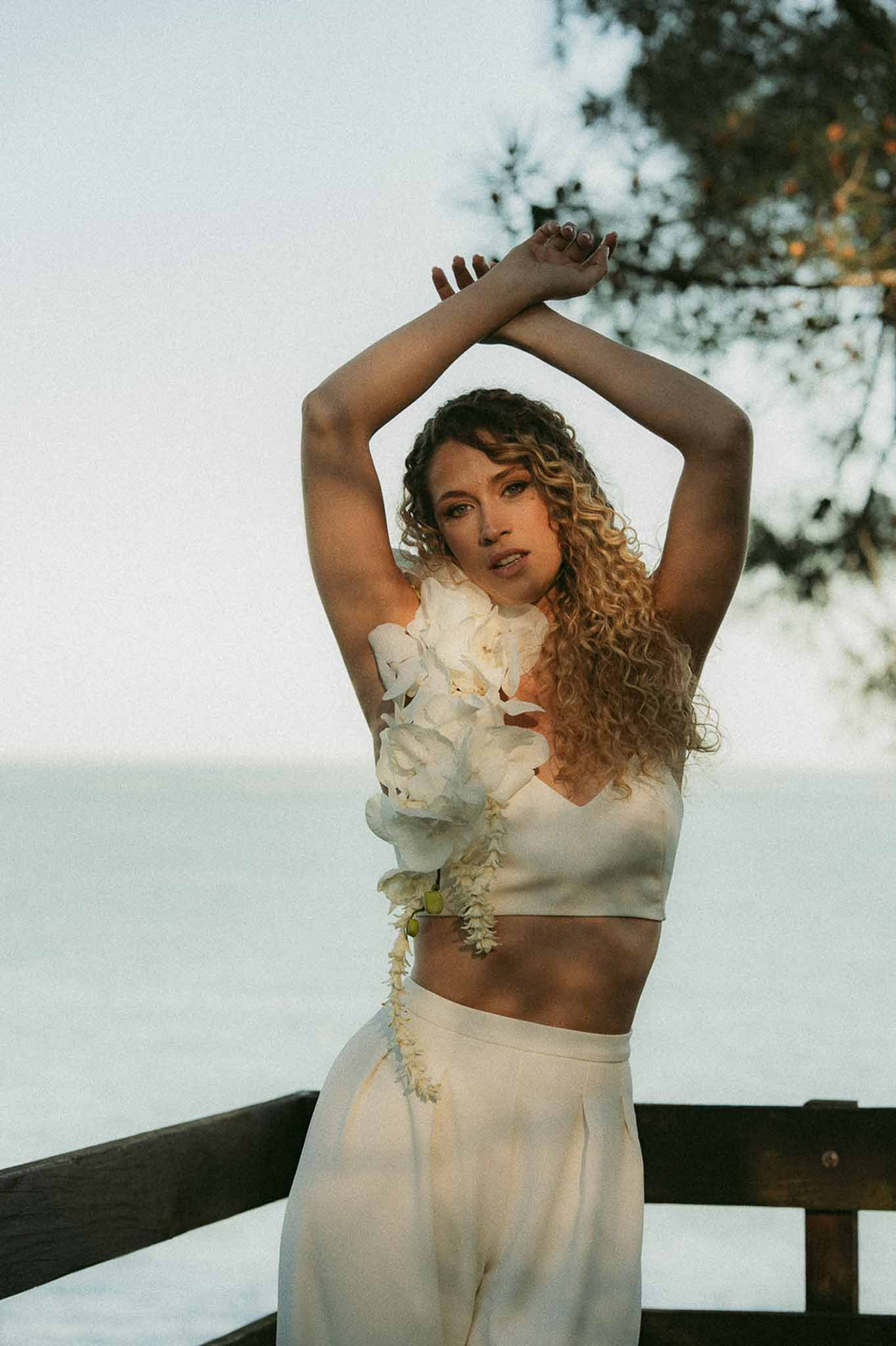 Bride in ivory crop top and wide-leg trousers with cascading white floral adornment on terrace