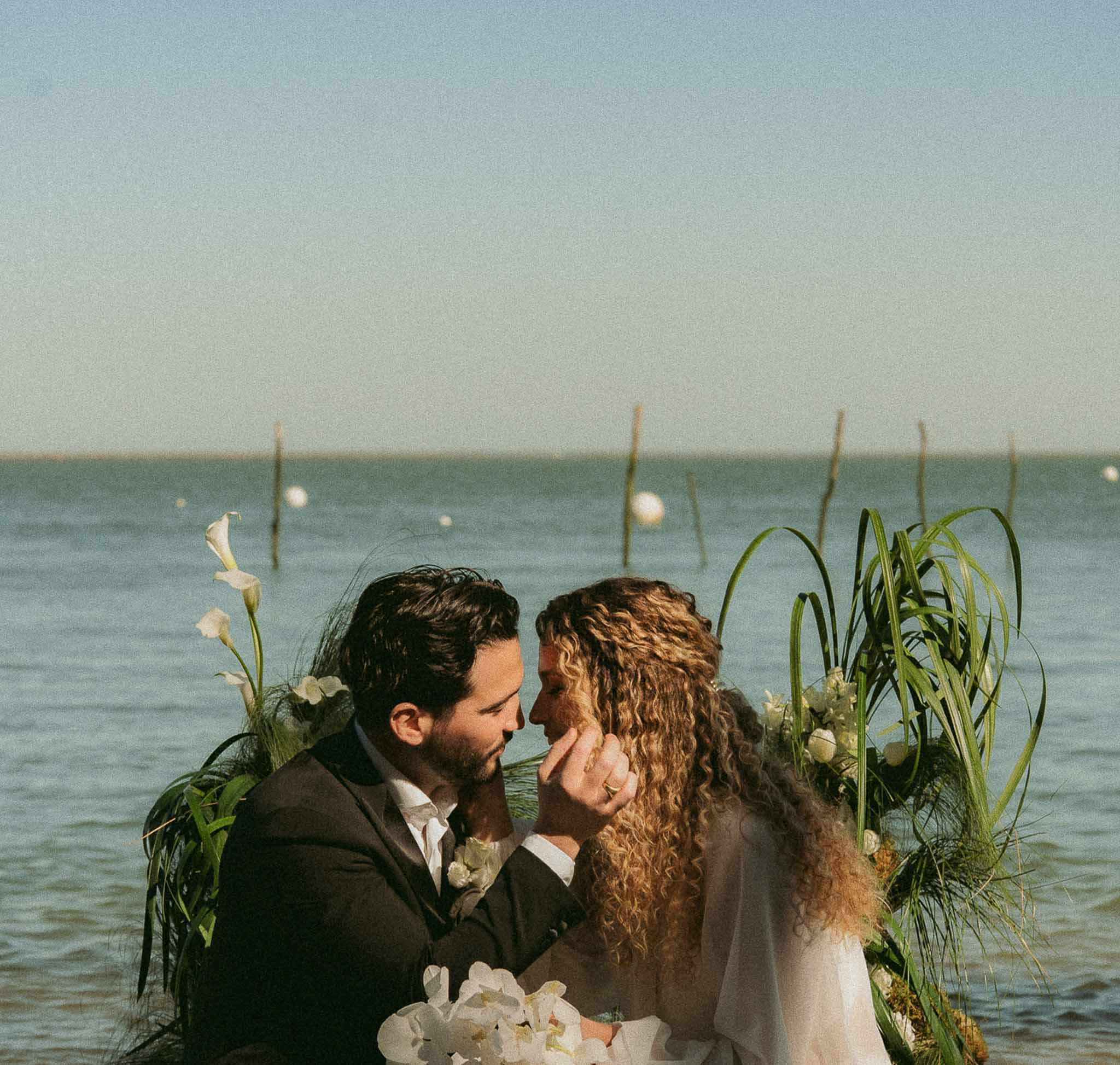 Groom lifts bride's chin at seaside ceremony arch of white calla lilies and hydrangeas with wooden posts