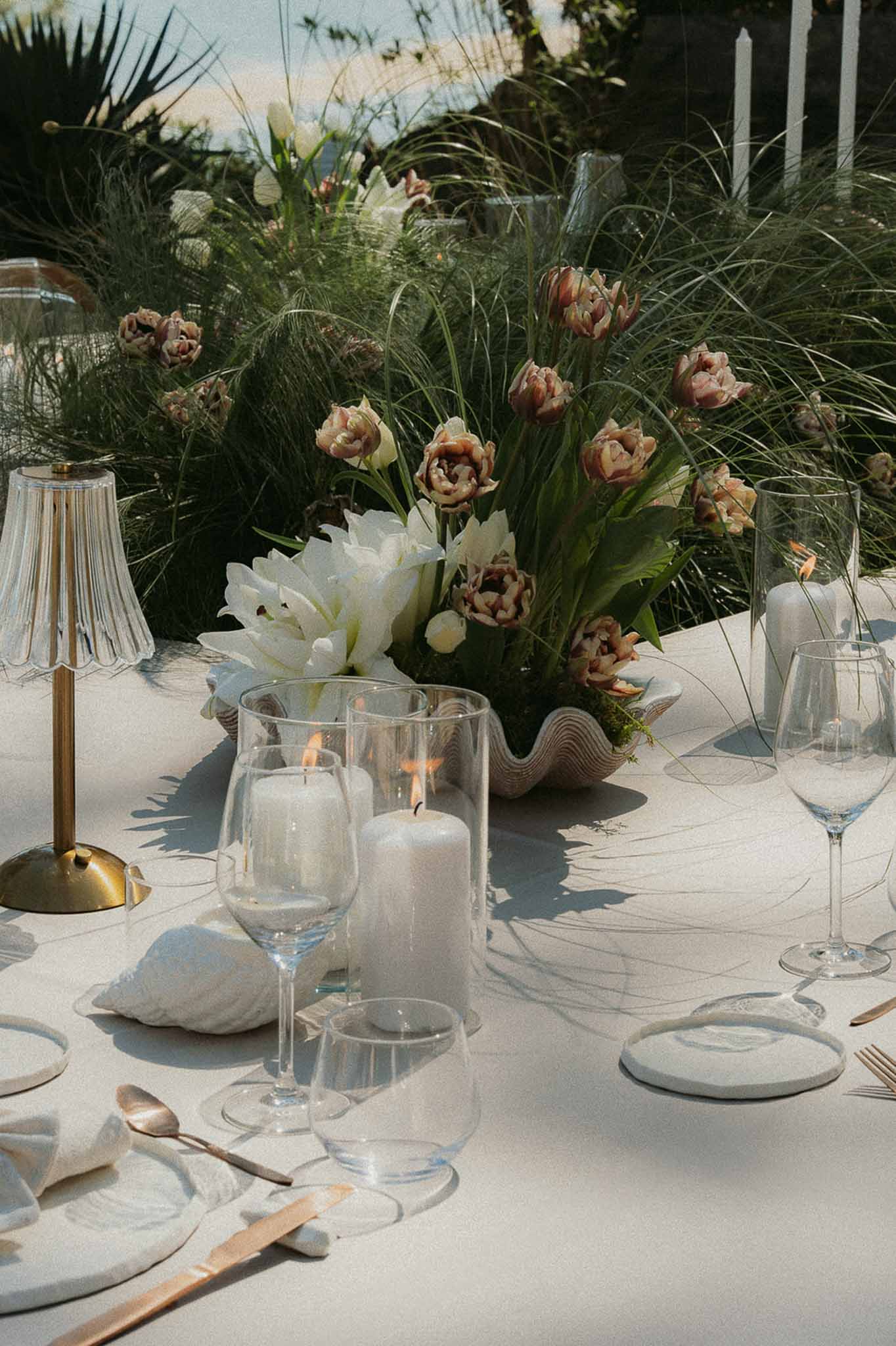 Shell-shaped vessel with white amaryllis and mauve tulips, hurricane candles, and coastal-organic table setting