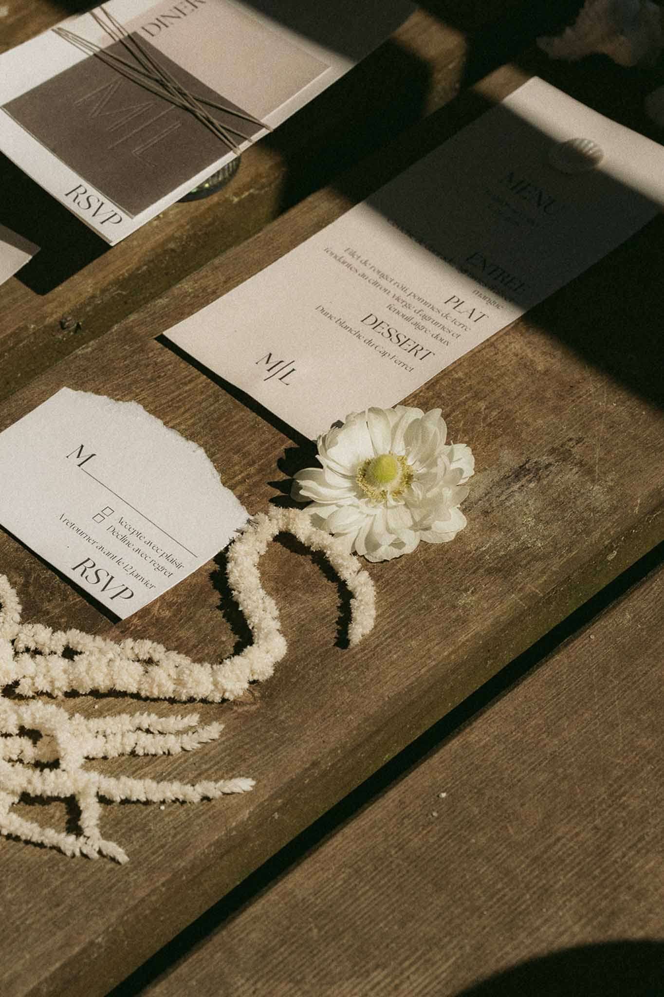 French wedding stationery flat lay with RSVP card, menu cards, and white bloom on weathered wood surface